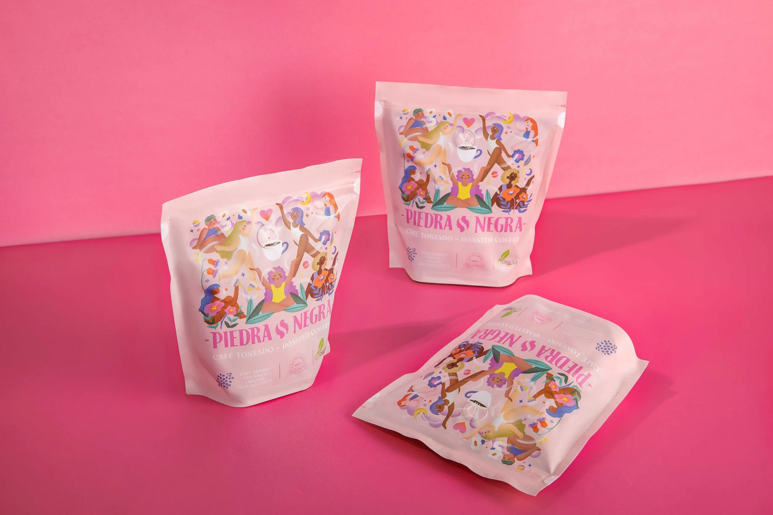 Tres paquetes de café tostado de color rosa con ilustraciones de personas en actividades alegres, sobre un fondo rosa.