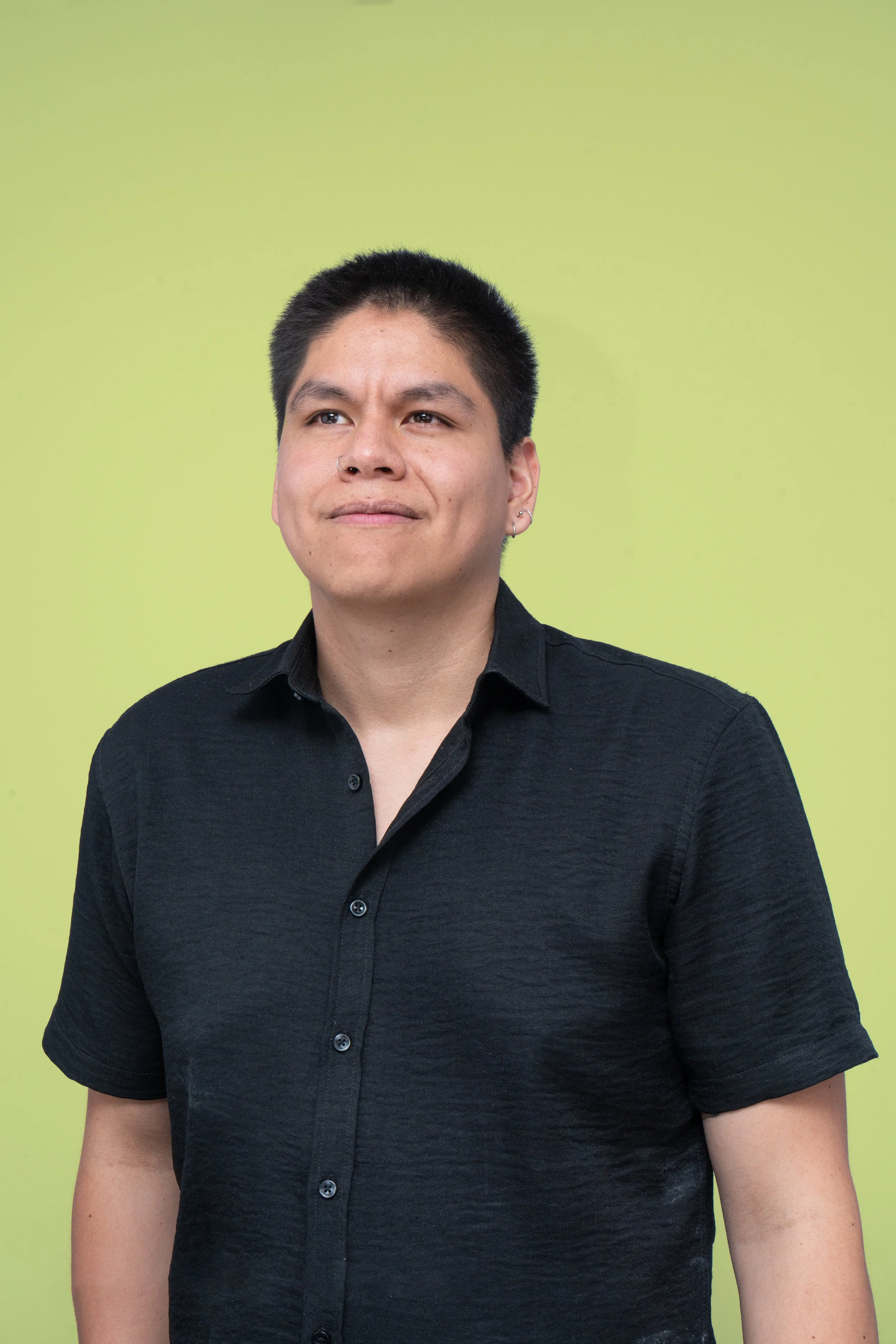 Joven hombre con cabello oscuro, usando camiseta negra, mira pensativo, fondo verde