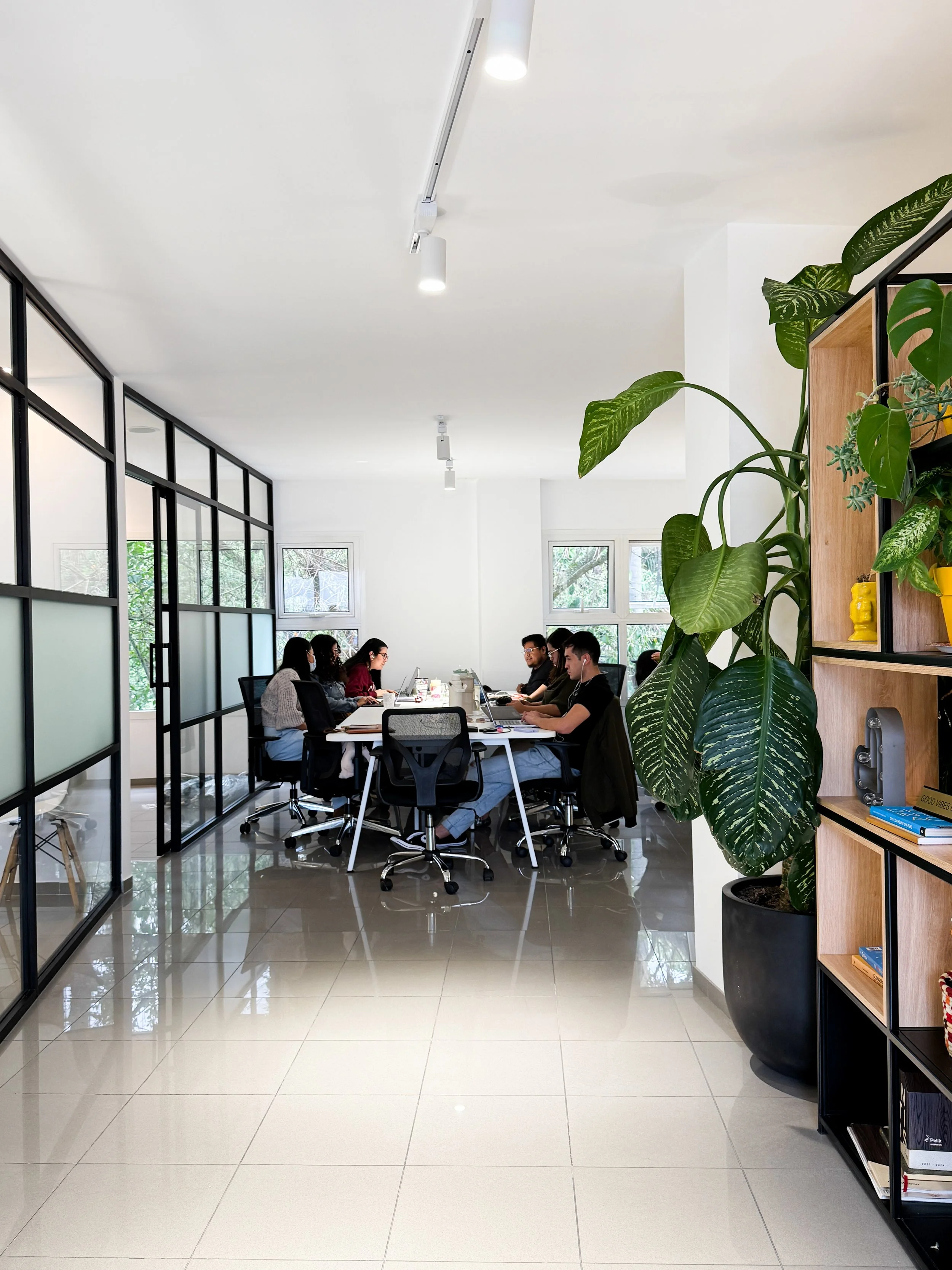 Grupo de personas trabajando en una oficina moderna con plantas y paredes de vidrio.