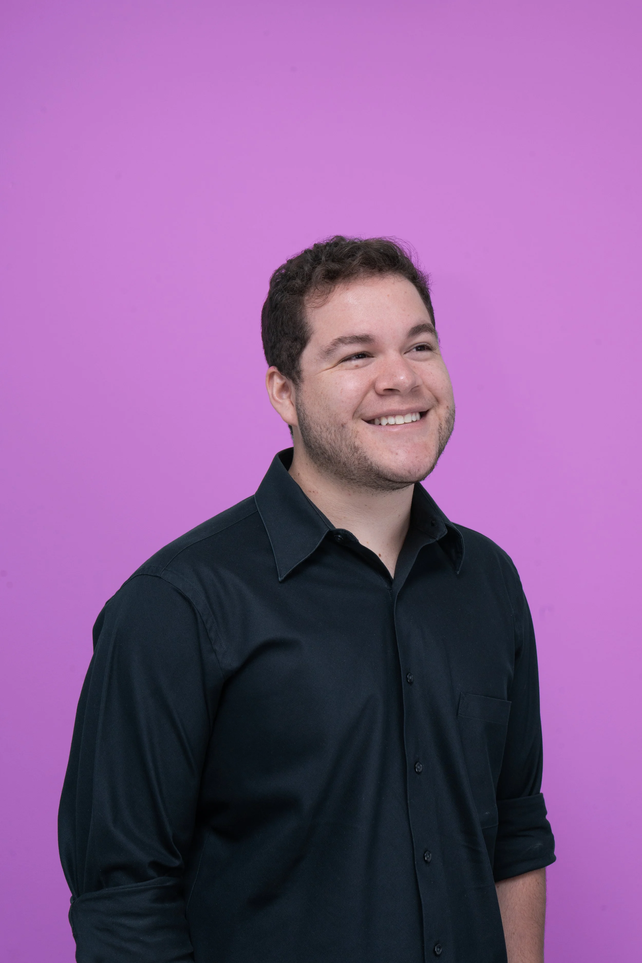 Joven con camiseta negra sonriendo en fondo rosa