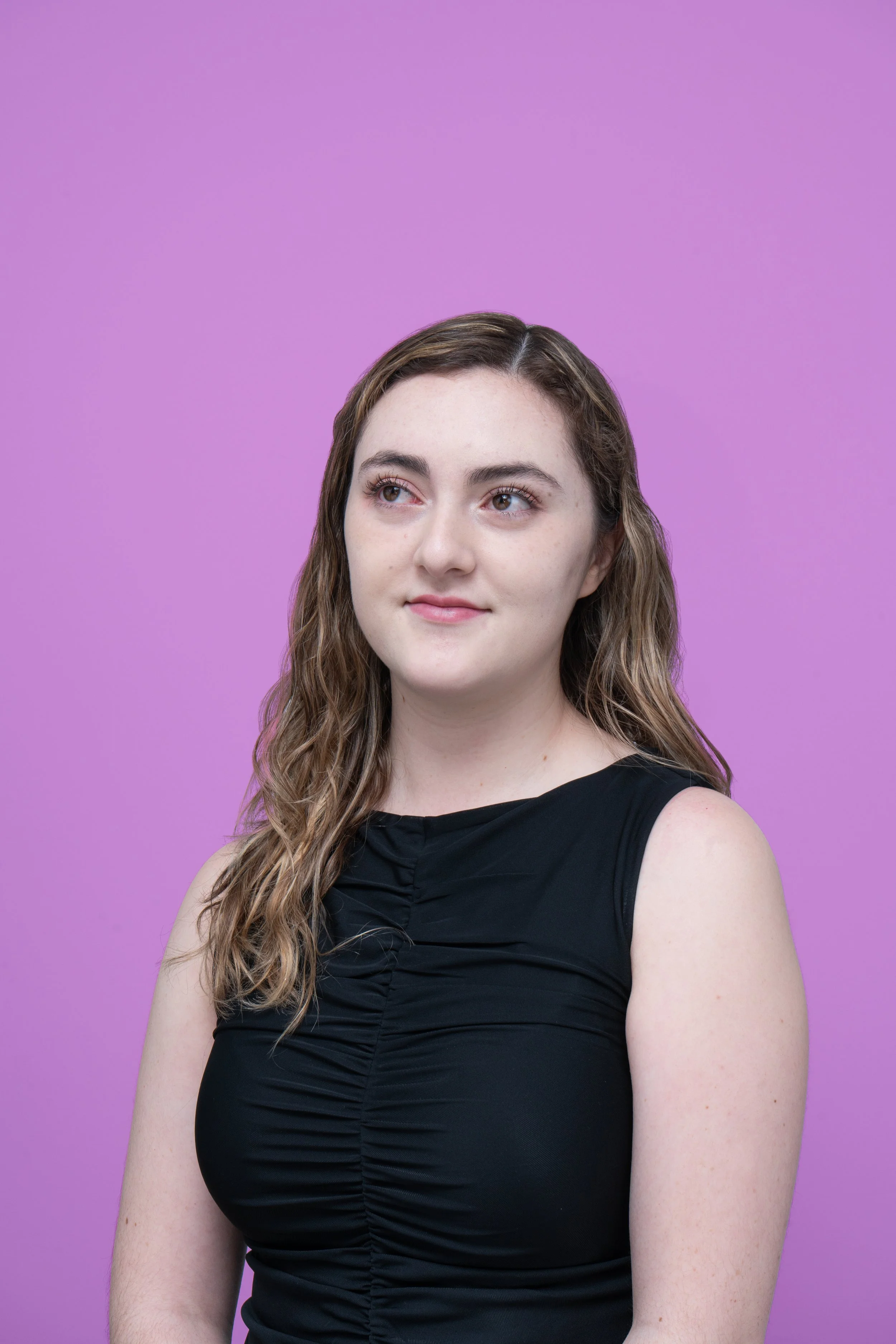Retrato de una joven con cabello castaño, ojos grandes y piel clara, vestida con blusa negra, frente a un fondo lila