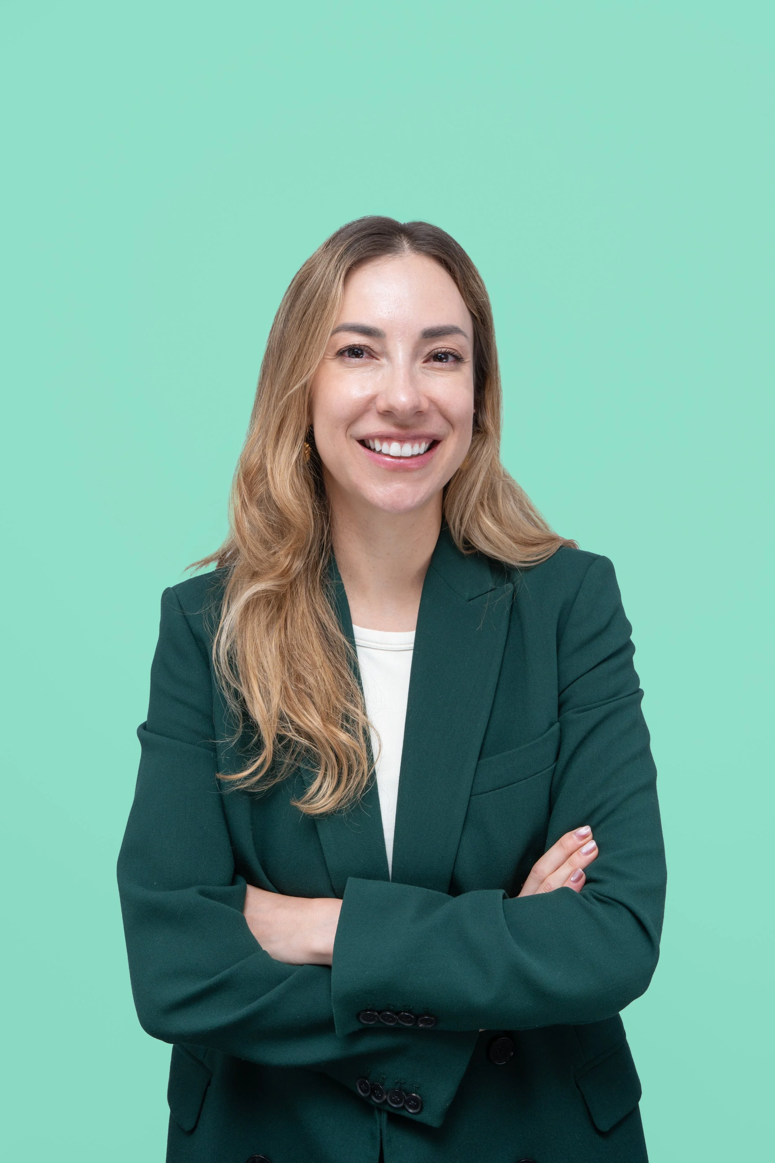 Mujer sonriente con cabello rubio y veste verde, brazos cruzados, fondo de color verde menta.