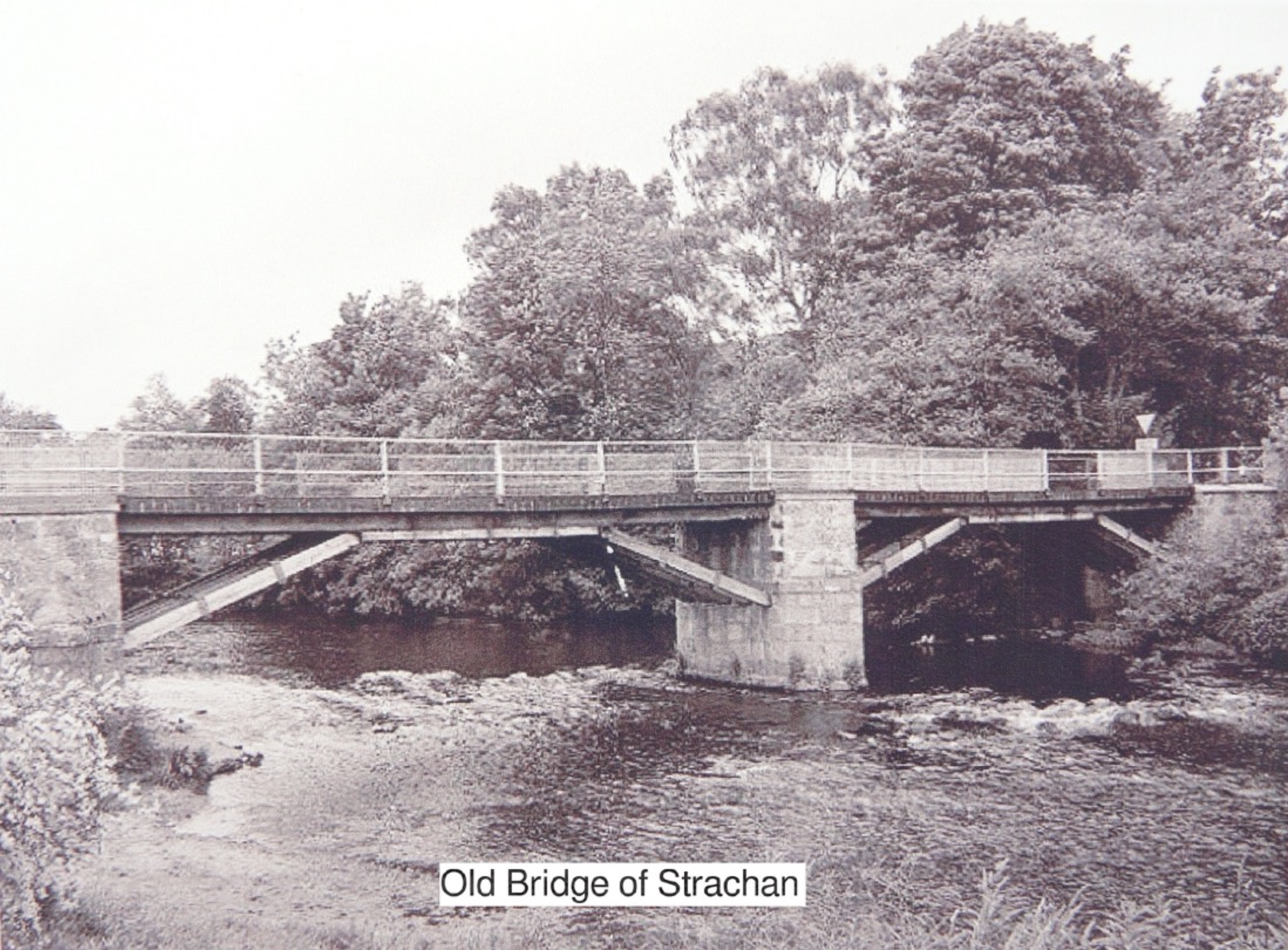A black-and-white photograph of the old bridge of Strachan, spanning over a river with trees in the background.