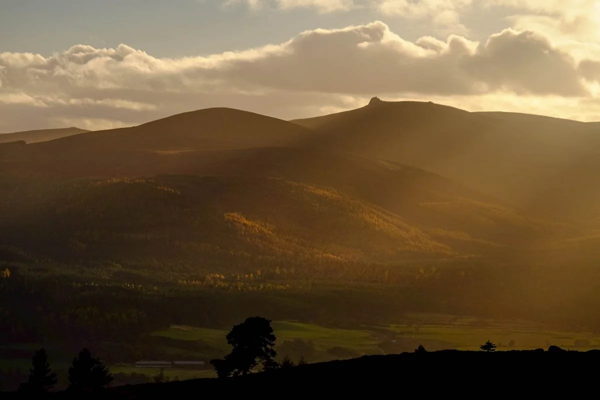 Sunset over rolling hills and mountains with a partly cloudy sky.