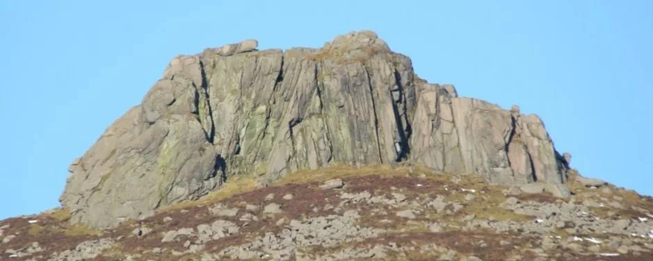 Close-up of a large rock formation on a hillside with a clear blue sky in the background.