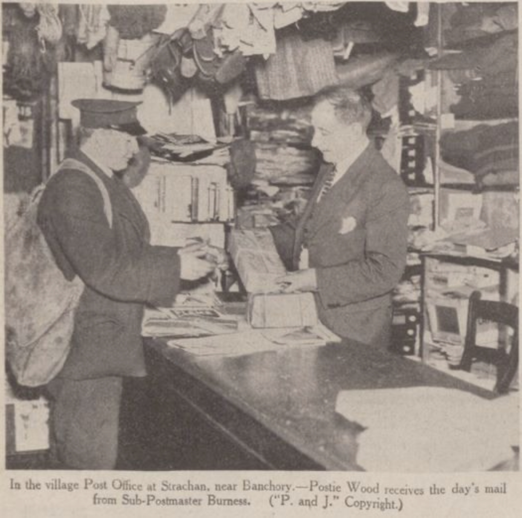 Two men inside a post office, one receiving mail from the other. The man on the right is in a military uniform, and the man on the left is dressed in a suit. The space is filled with shelves and boxes of mail.