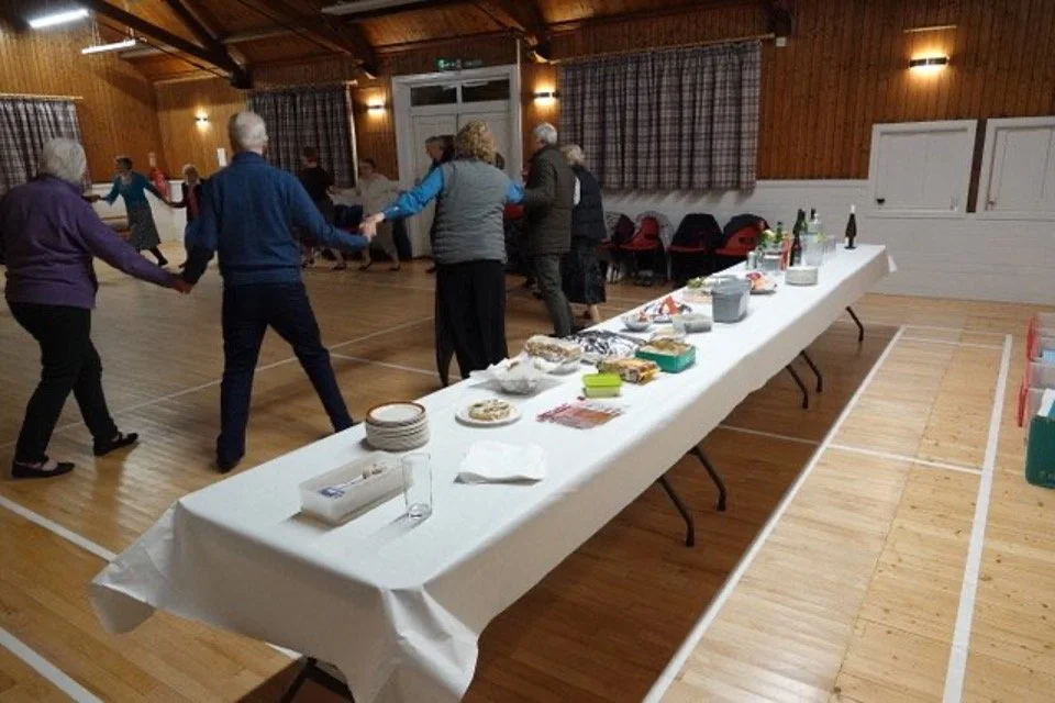 People dancing in a social gathering, with a table of snacks and drinks set up in Strachan Hall.