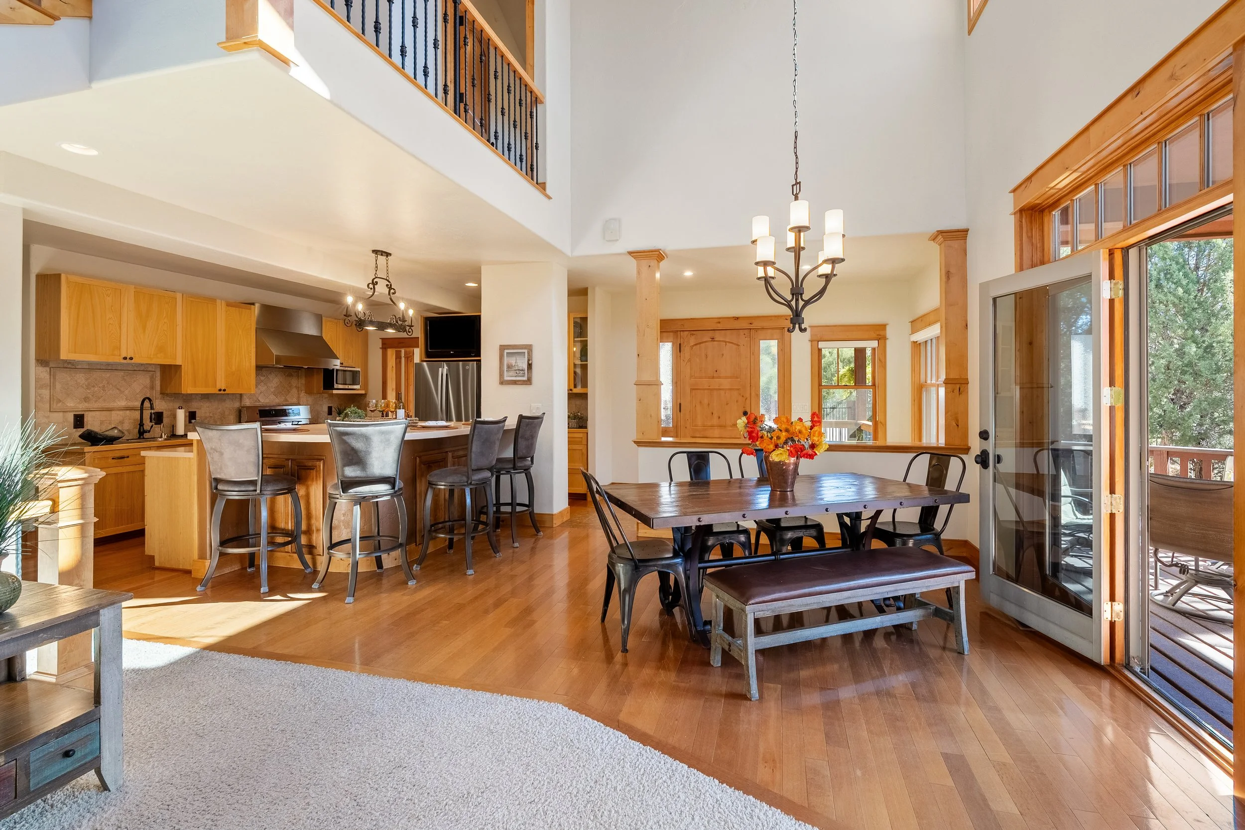Open-concept living space with a kitchen and dining area, featuring wooden cabinets, a stainless steel refrigerator, a dining table with chairs, and large windows and glass door leading to an outdoor deck.