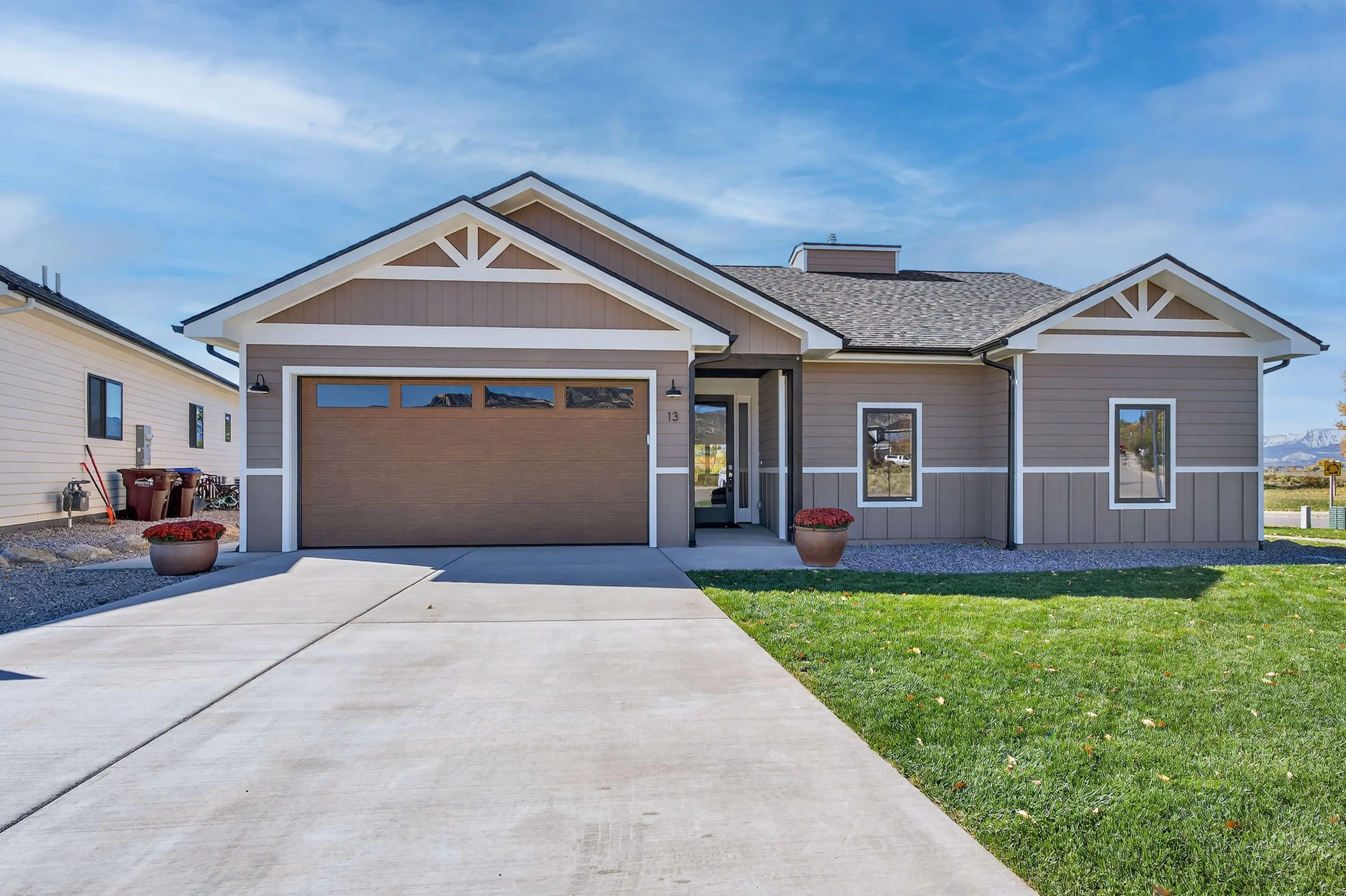 Modern suburban house with a two-car garage, front walkway, and green lawn under a blue sky.