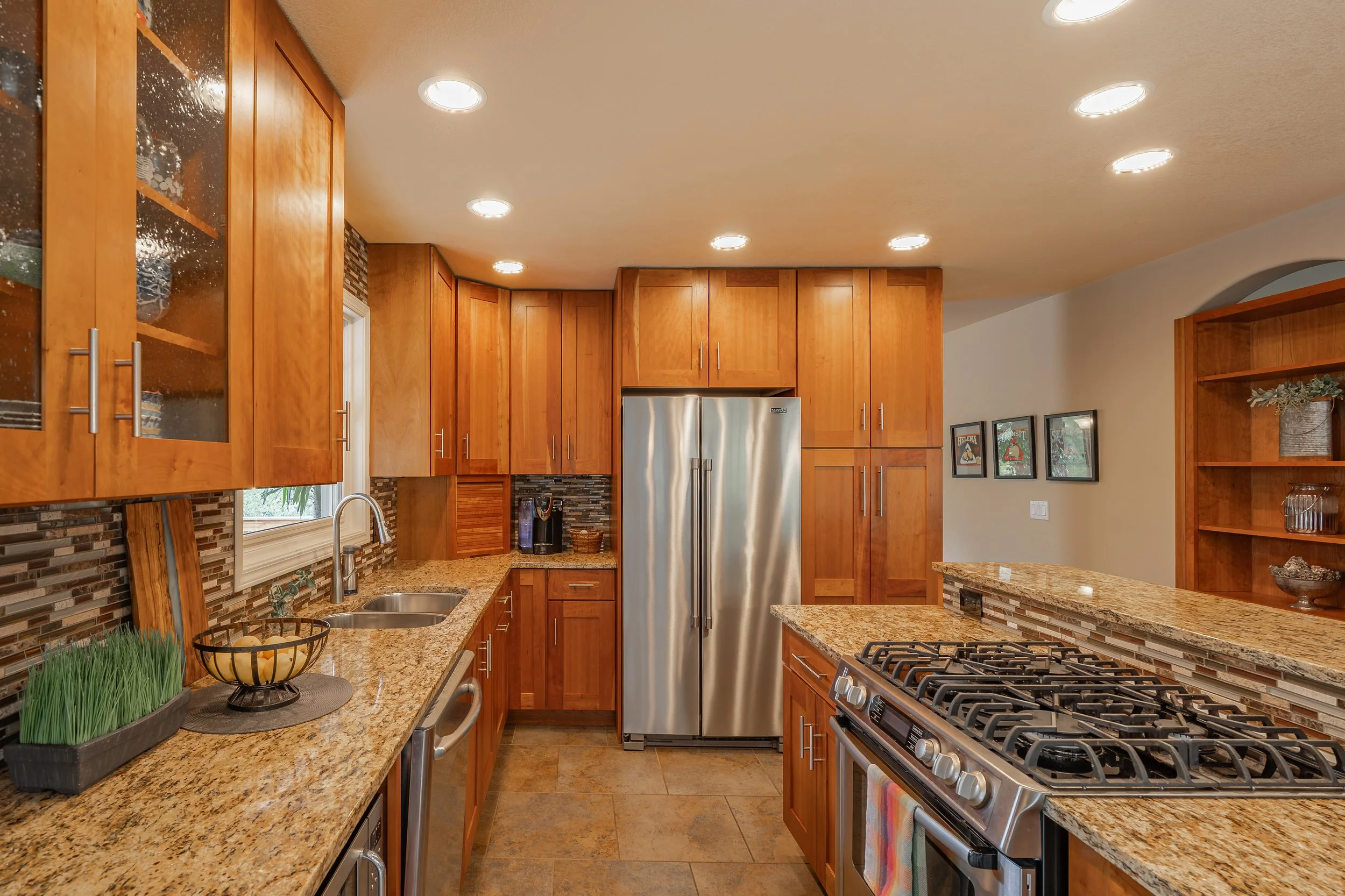 Modern kitchen with wooden cabinets, granite countertops, stainless steel refrigerator, gas stove, and decorative backsplash.