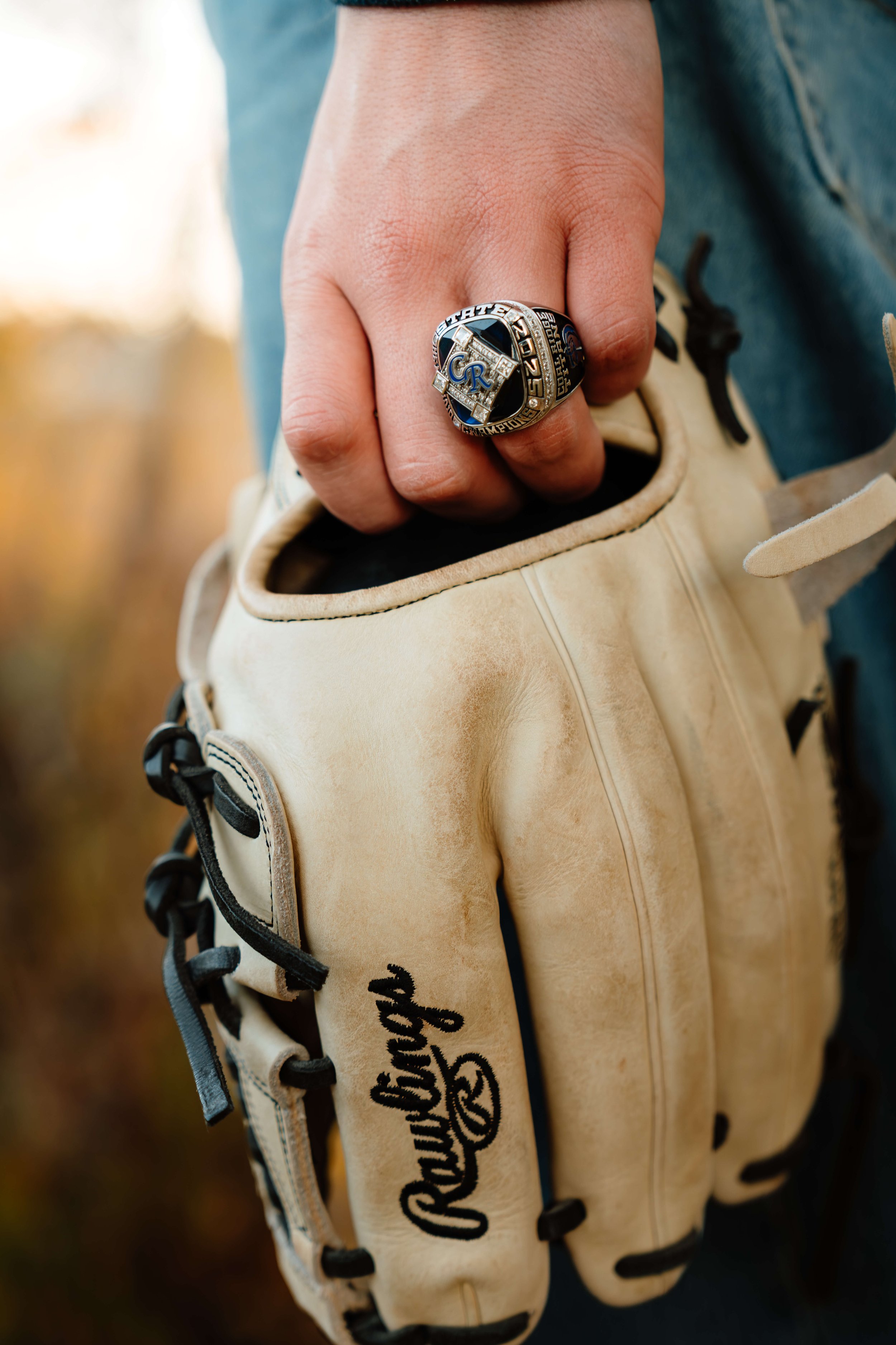 Close-up of a person's hand wearing a championship baseball ring on their finger, casually resting on a Rawlings baseball glove.