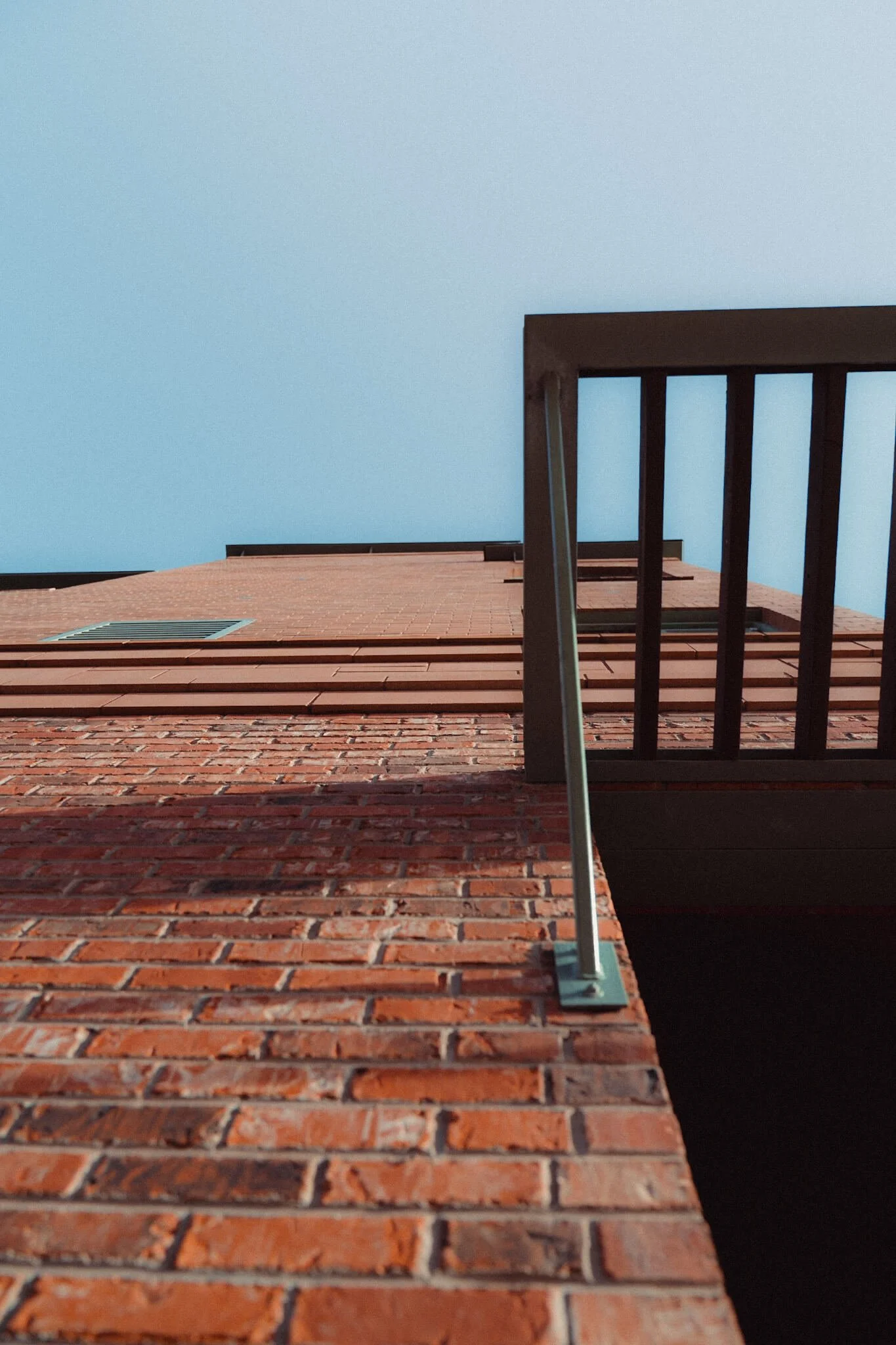 Low-angle view of a brick building corner with a metal railing and a clear blue sky.