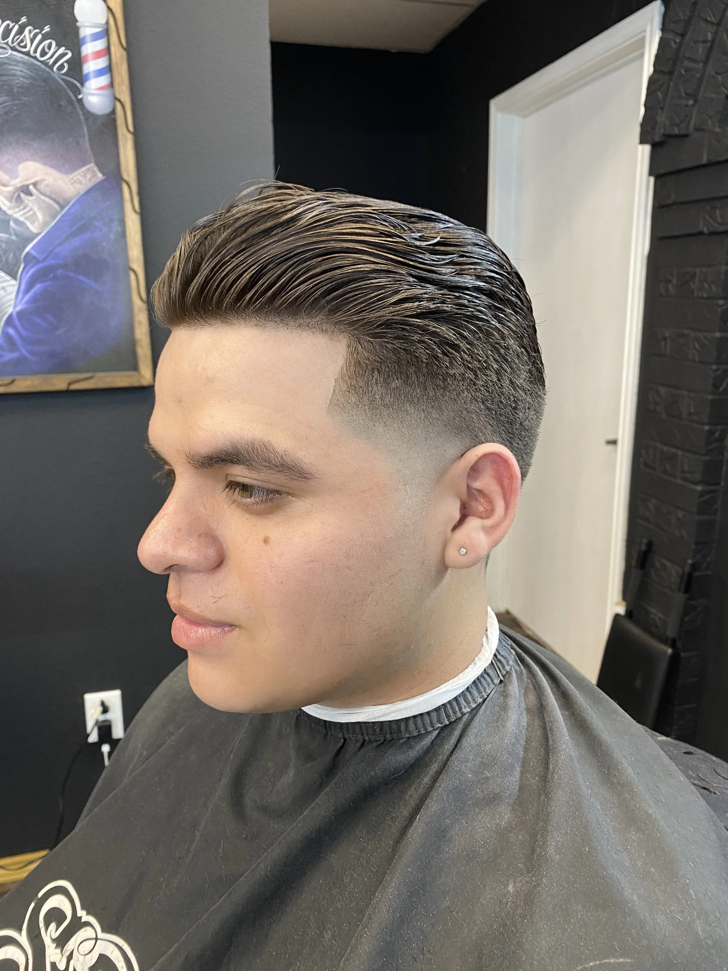 Young man with a classic slicked-back hairstyle getting a professional haircut at a barbershop.