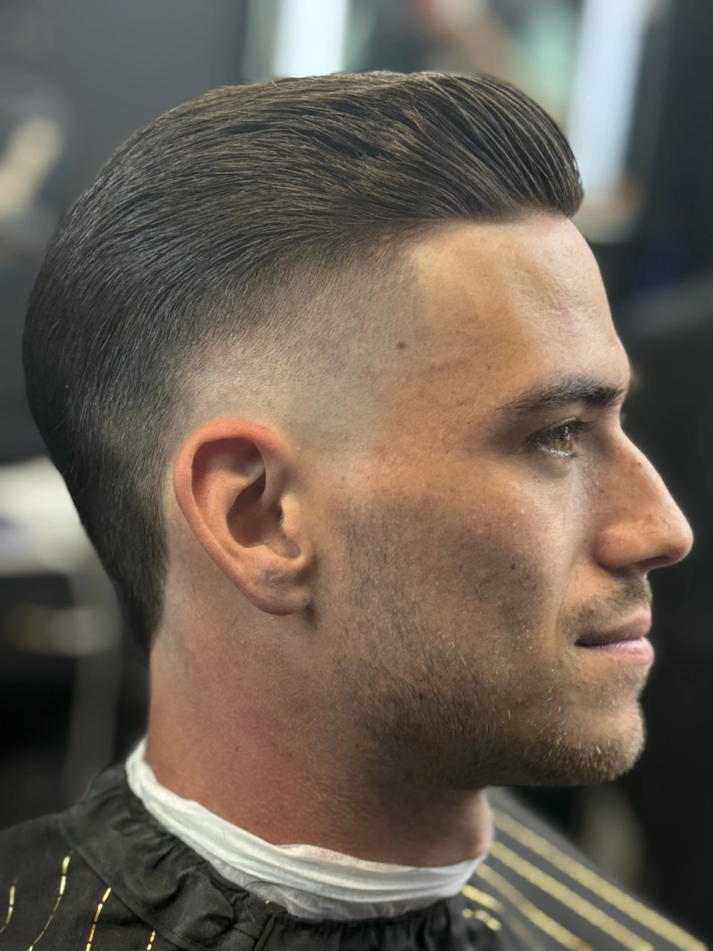 Side profile of a man with a neat, slicked-back hairstyle and a fade haircut at a barbershop.