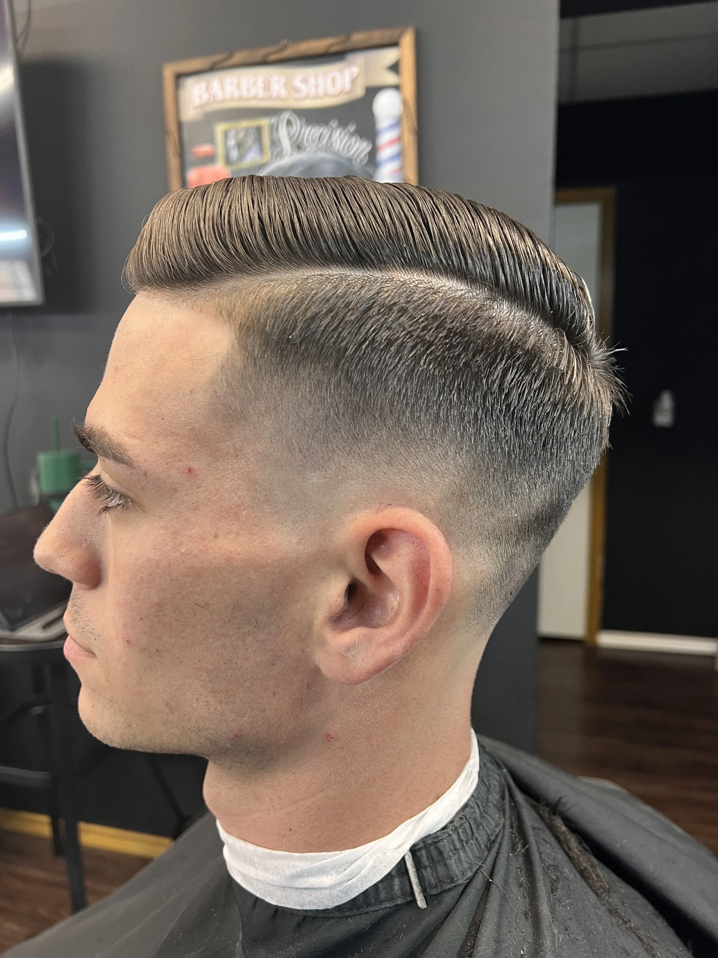 Man with a classic animated hairstyle in a barbershop, featuring a fade haircut with longer hair slicked back on top.