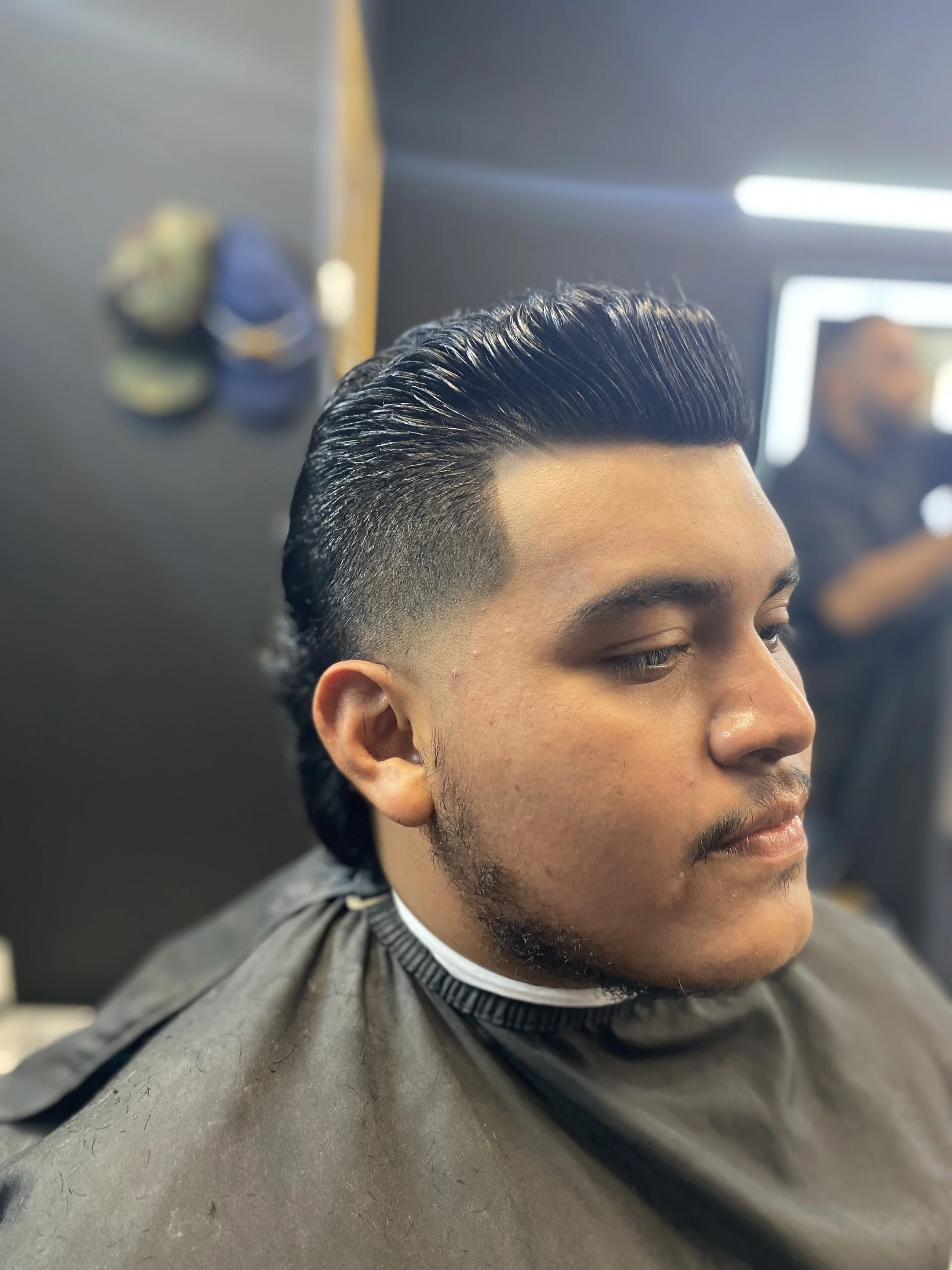 Young man with a freshly styled, slicked back haircut getting a haircut in a barbershop.