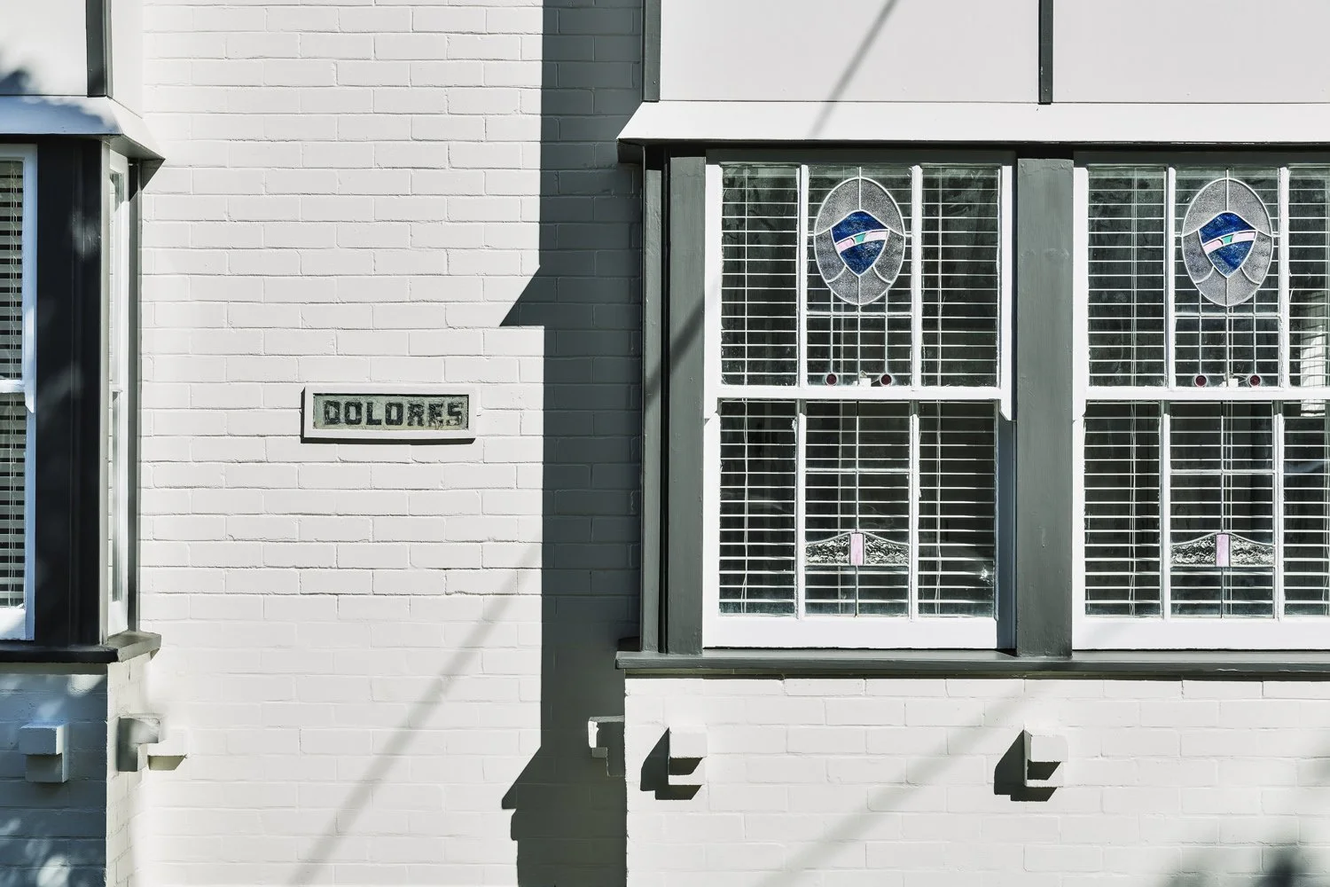 Close-up of a white brick building with two stained glass windows and a sign that reads 'Dolores' on the wall.