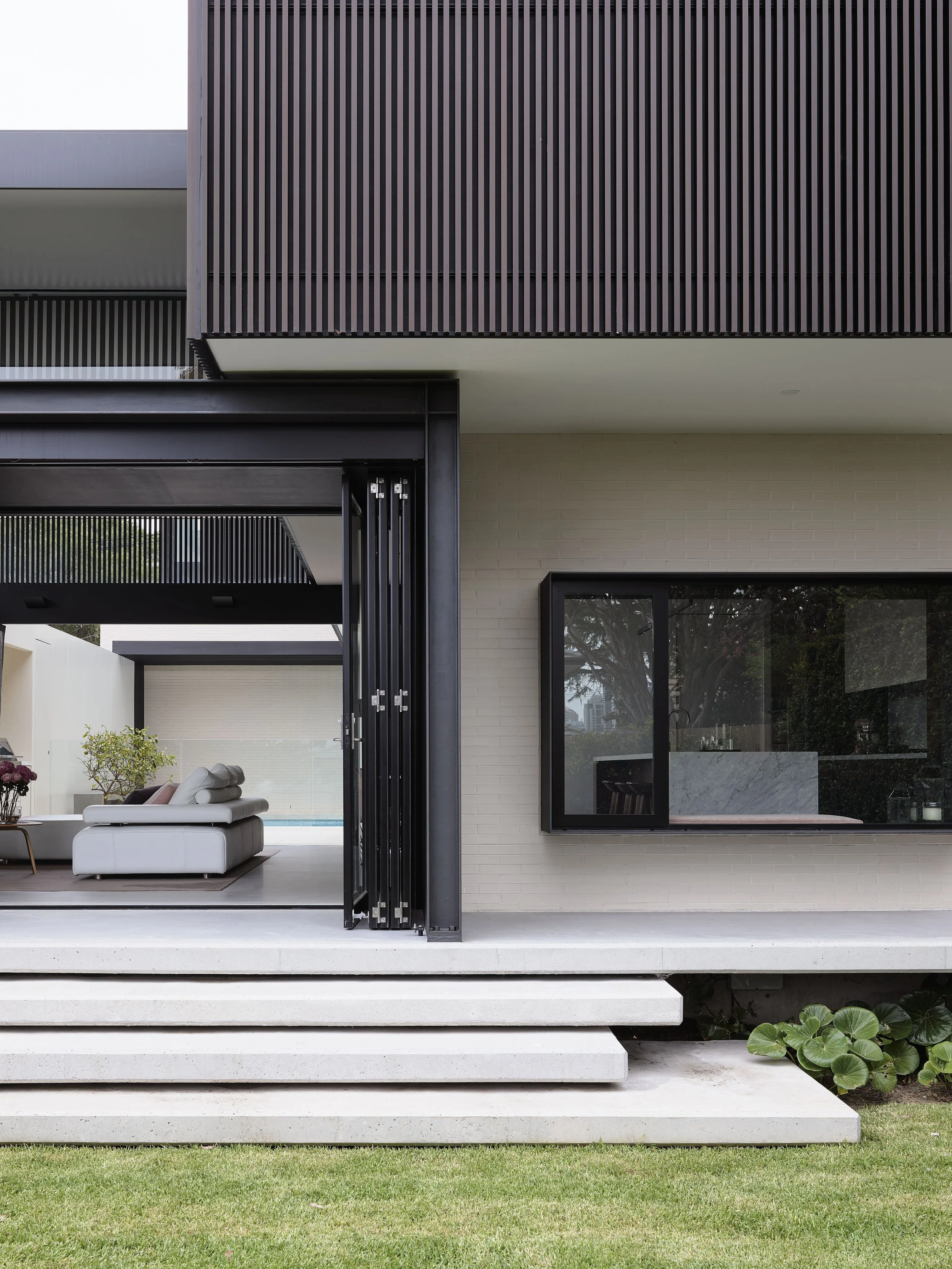 Modern house with a patio, open sliding door, white sofa, and a view of a pool in the backyard.