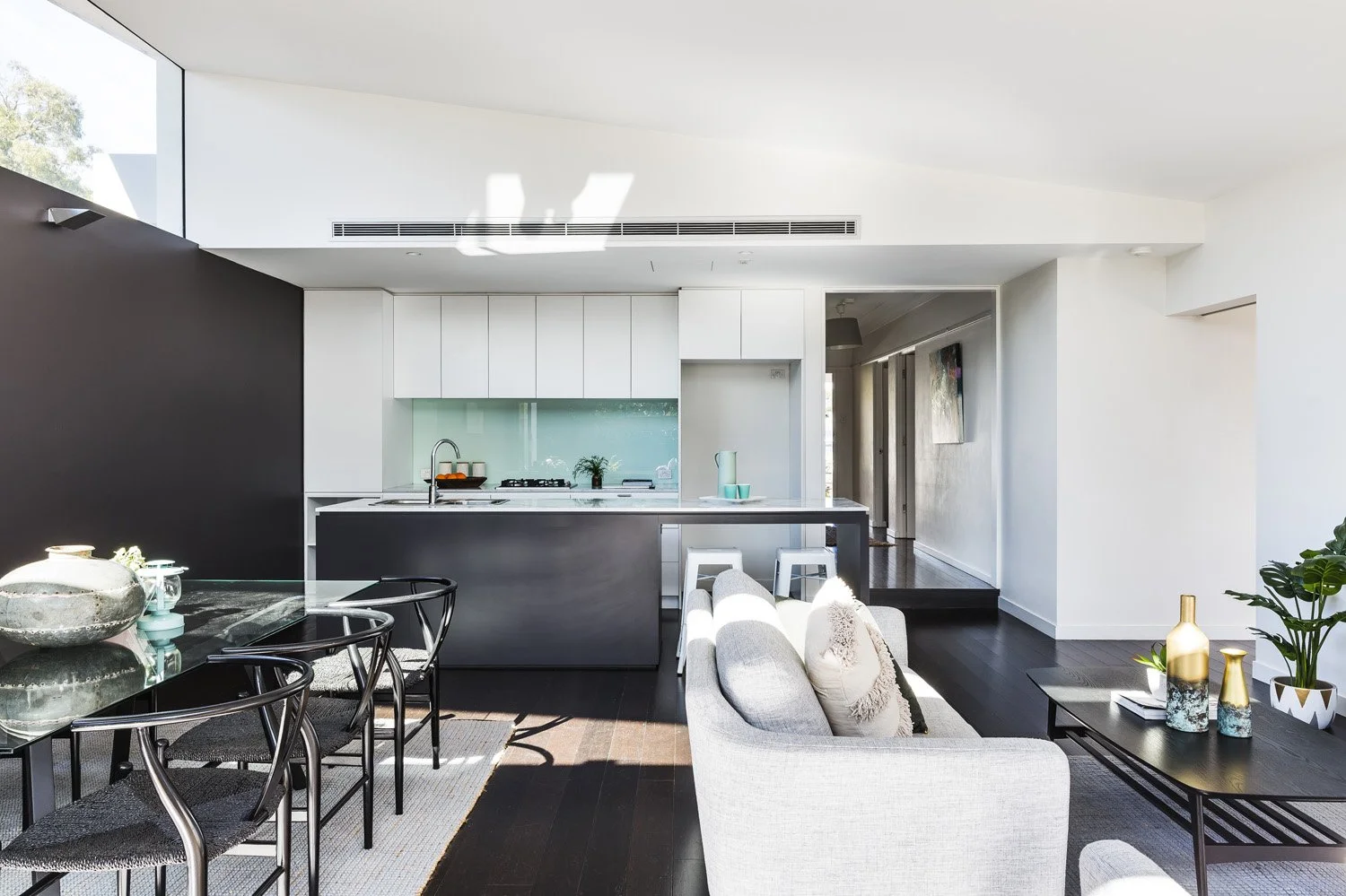 Modern open-concept living room and kitchen with white and black decor, dark hardwood floors, and large windows letting in natural light.