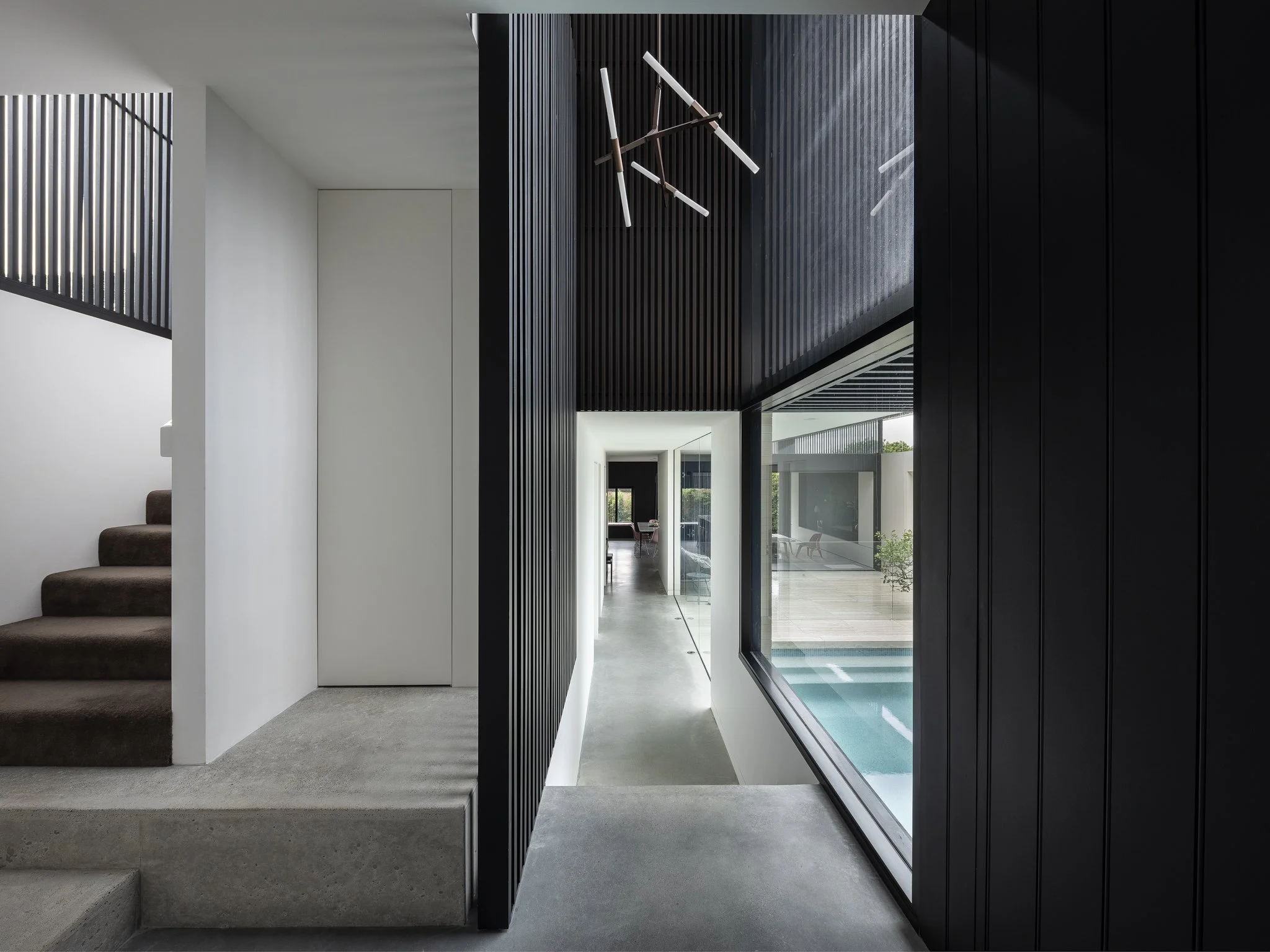 Modern interior with staircase, black wooden walls, large window overlooking outdoor pool, contemporary chandelier, and minimalist decor