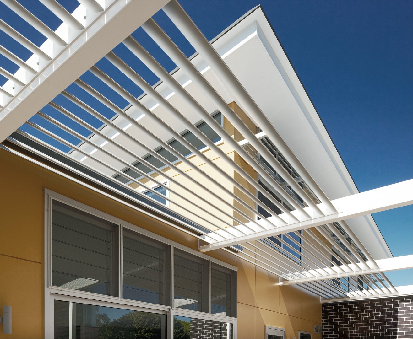Modern building with white horizontal slats and large windows, under a clear blue sky.