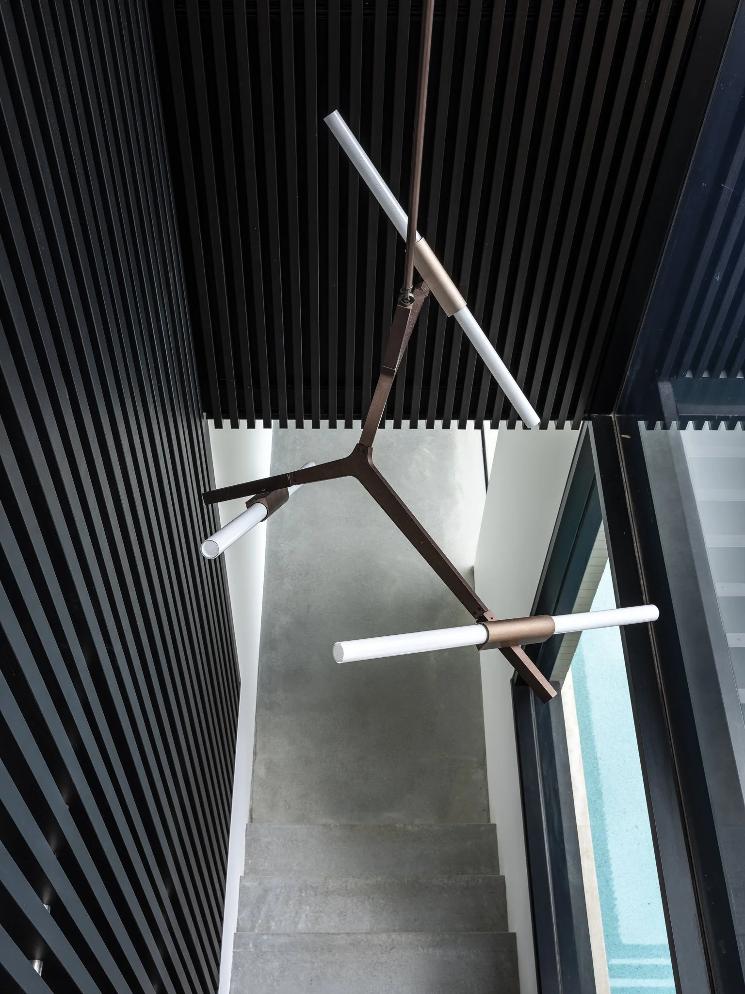 Modern staircase with black panel wall on one side and glass railing on the other, viewed from above.