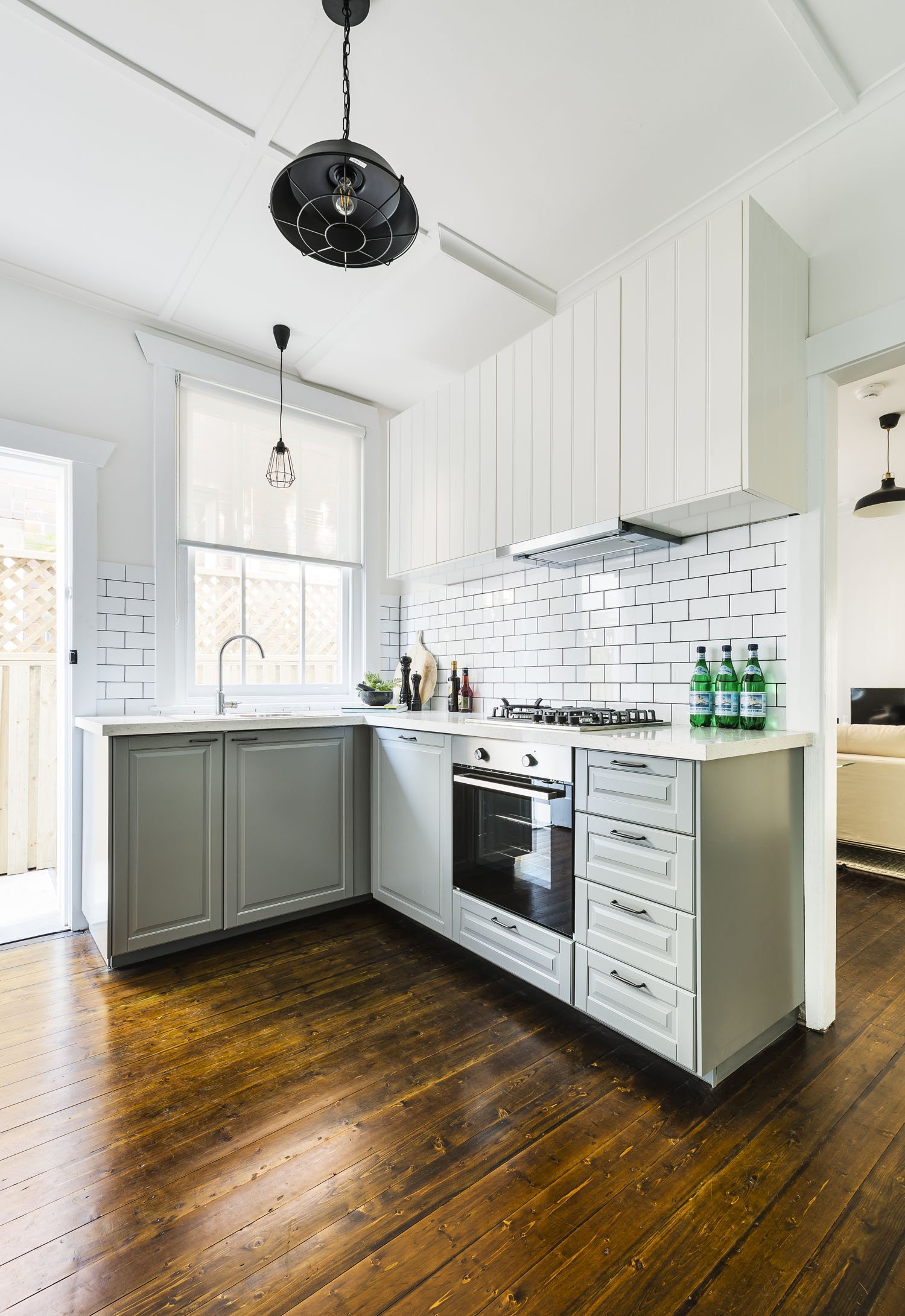 Modern kitchen with white cabinetry, white subway tile backsplash, dark wood floors, and black pendant lighting.
