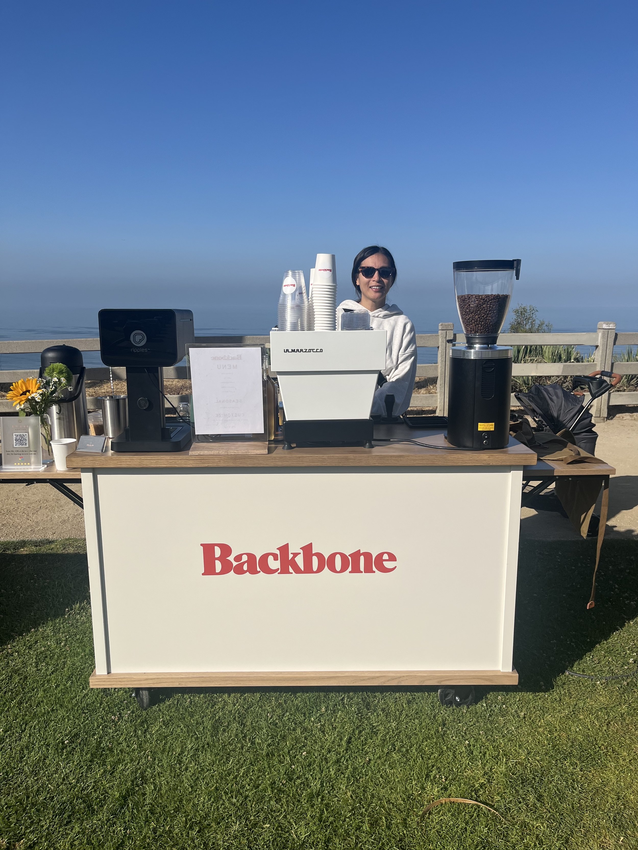 Pulo Coffee smiling barista at a custom branded Backbone mobile matcha bar and espresso cart at an outdoor event in Los Angeles
