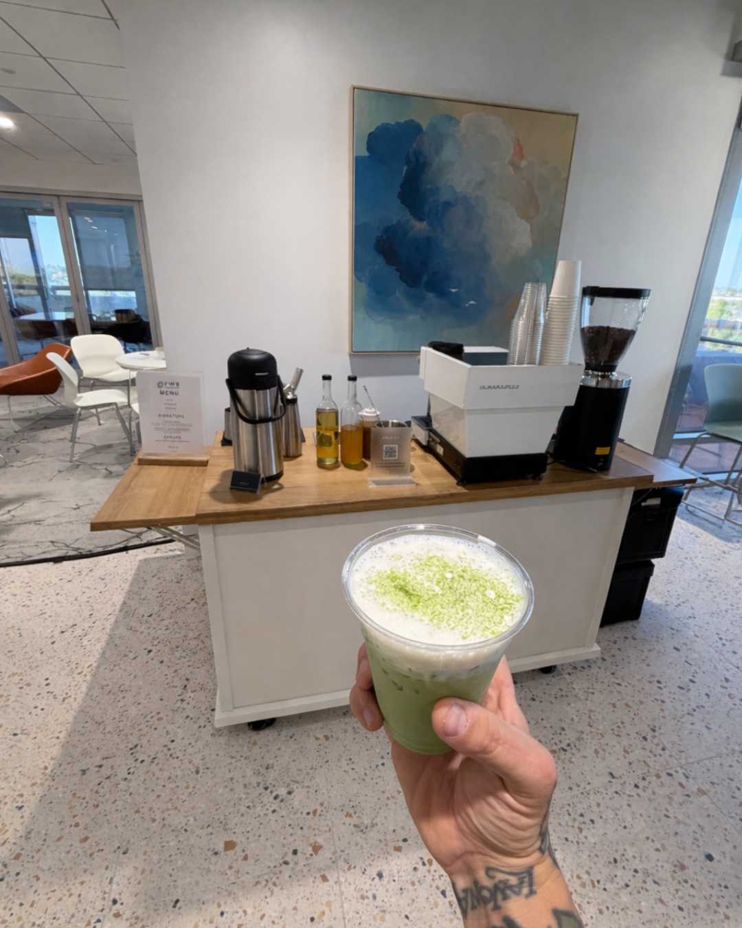Iced matcha latte with matcha powder cold foam held in front of a Pulo Coffee mobile matcha bar setup at a corporate event in Los Angeles