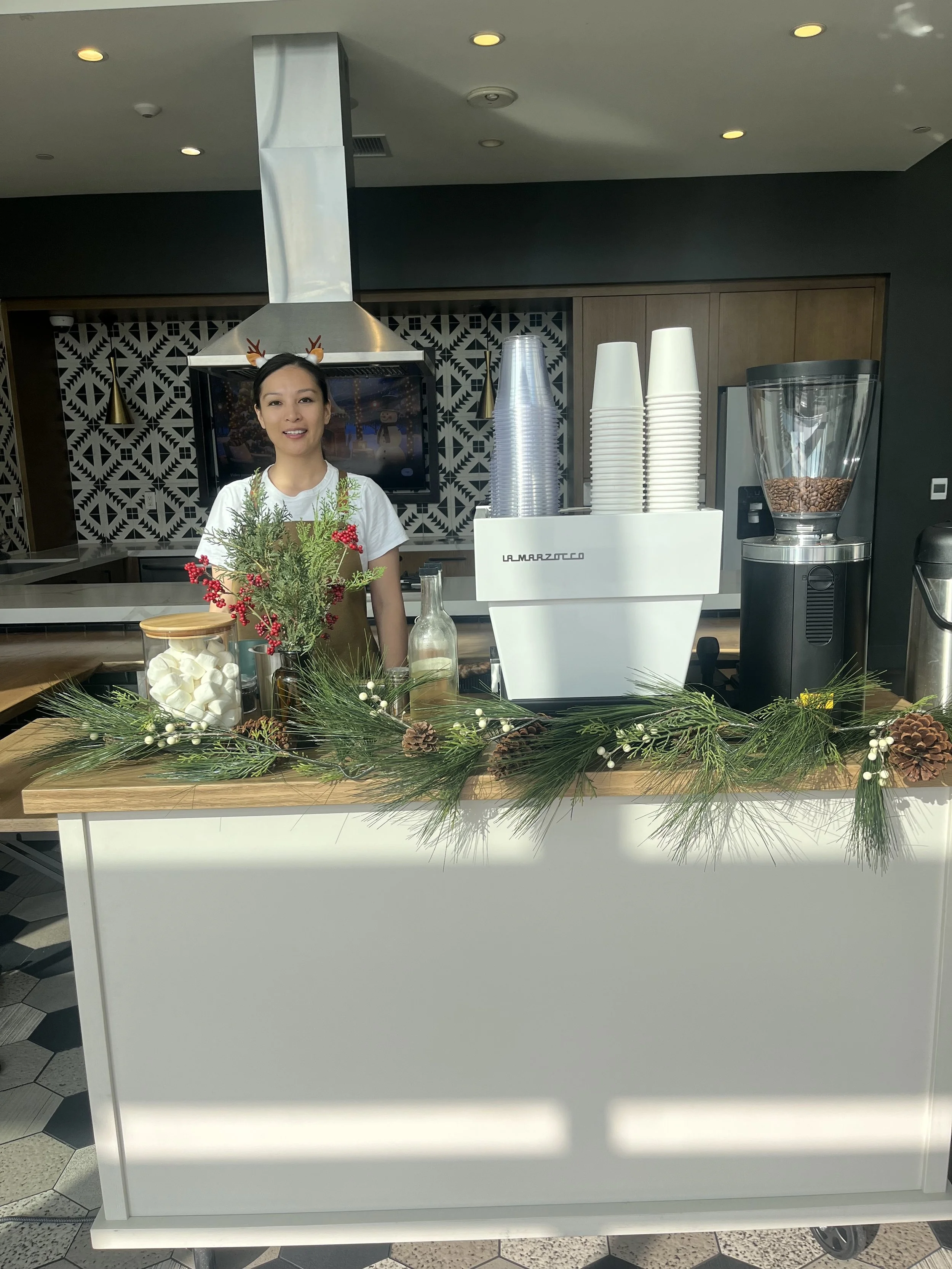 Pulo Coffee barista behind a holiday-decorated hot chocolate cart with pine garland, marshmallows, and seasonal florals at a Los Angeles catering event
