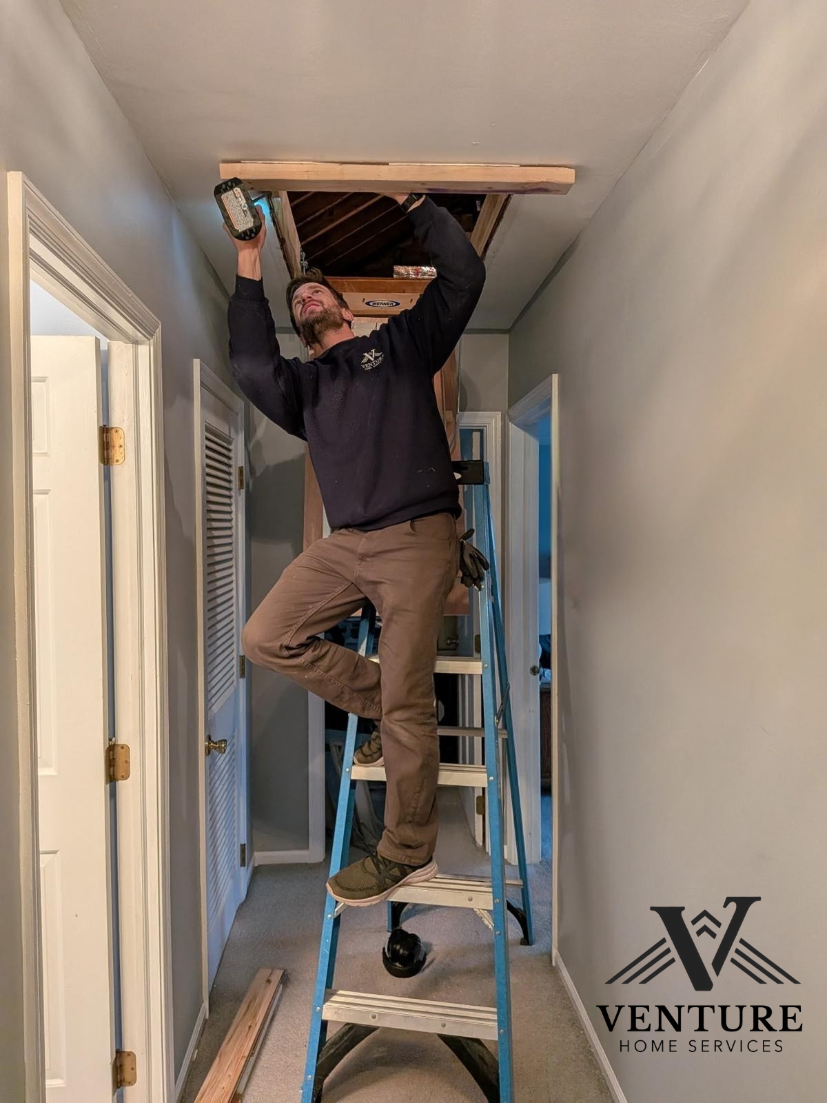 A man standing on a ladder working on an attic access in a hallway, holding a tool, with the logo of Venture Home Services in the bottom right corner.
