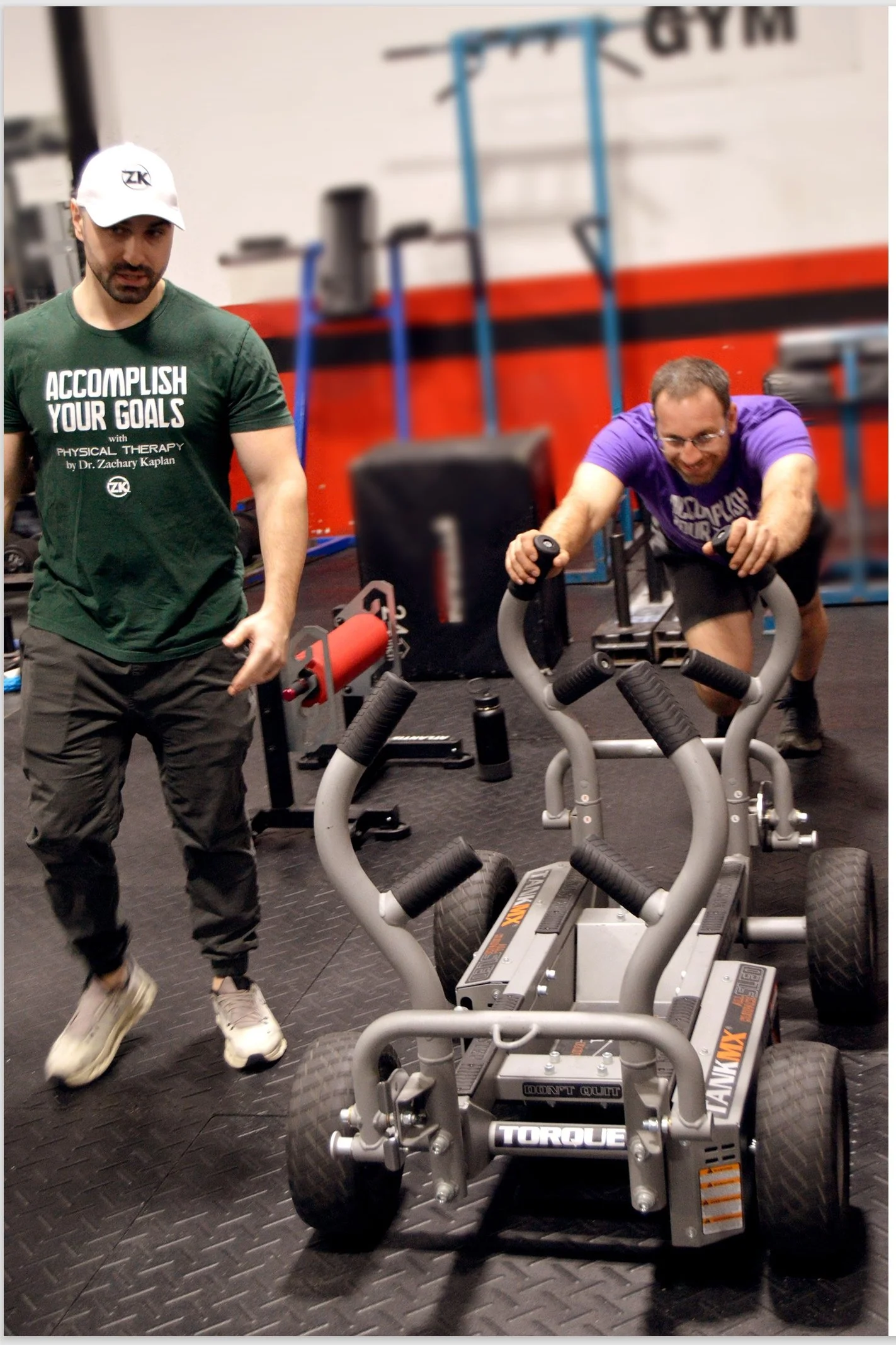 Client pushing a strength machine at the gym with Dr. Zach Kaplan at one side guiding the client