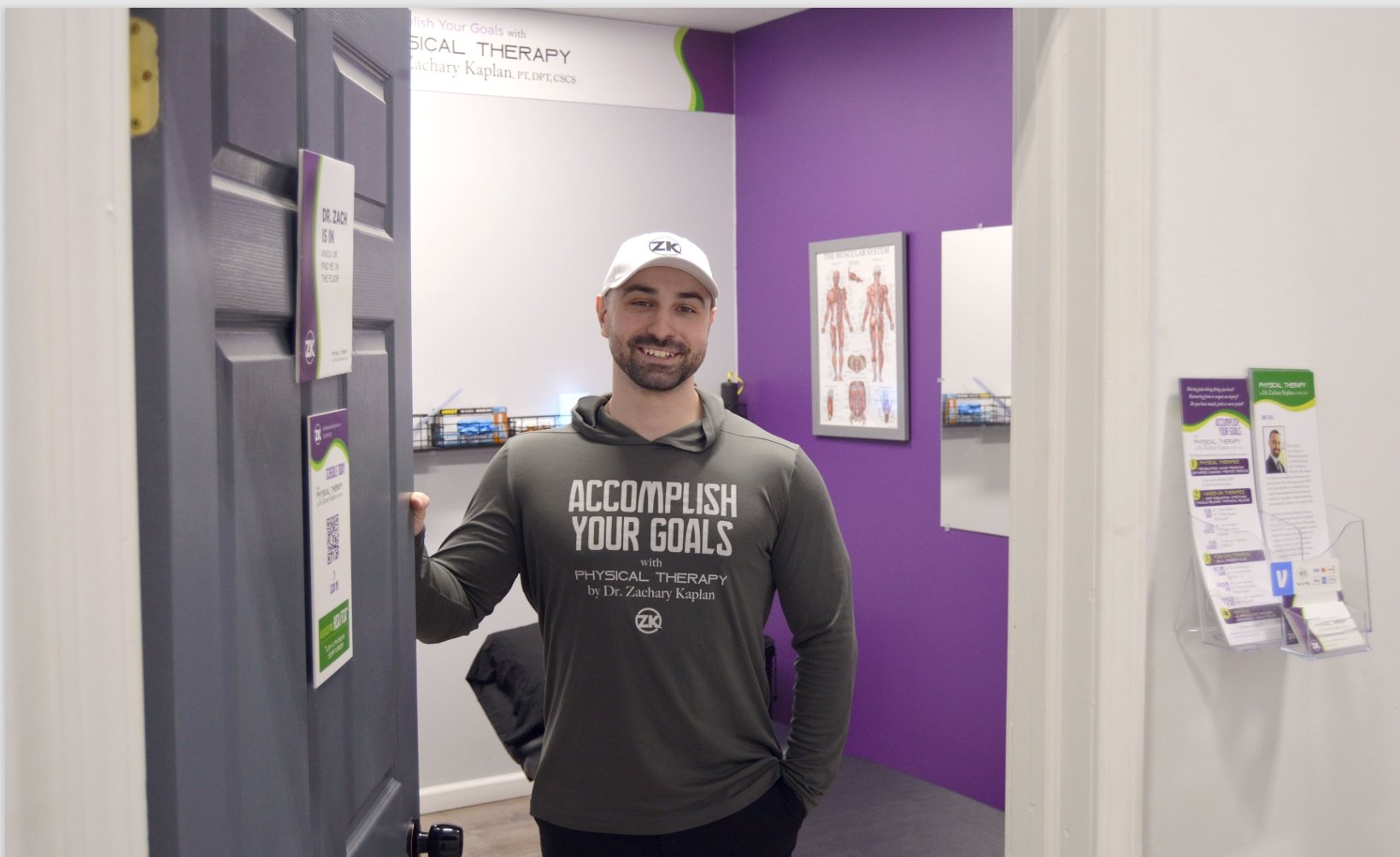 Dr. Zach Kaplan standing in the doorway of his office holding the door open