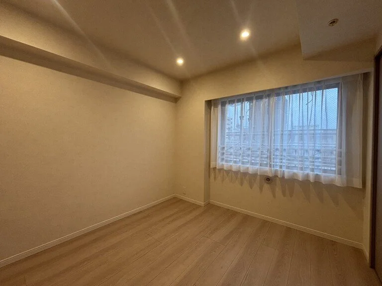 空室の部屋、木製の床と白い壁、窓にカーテン、夜の都市の景色が見える