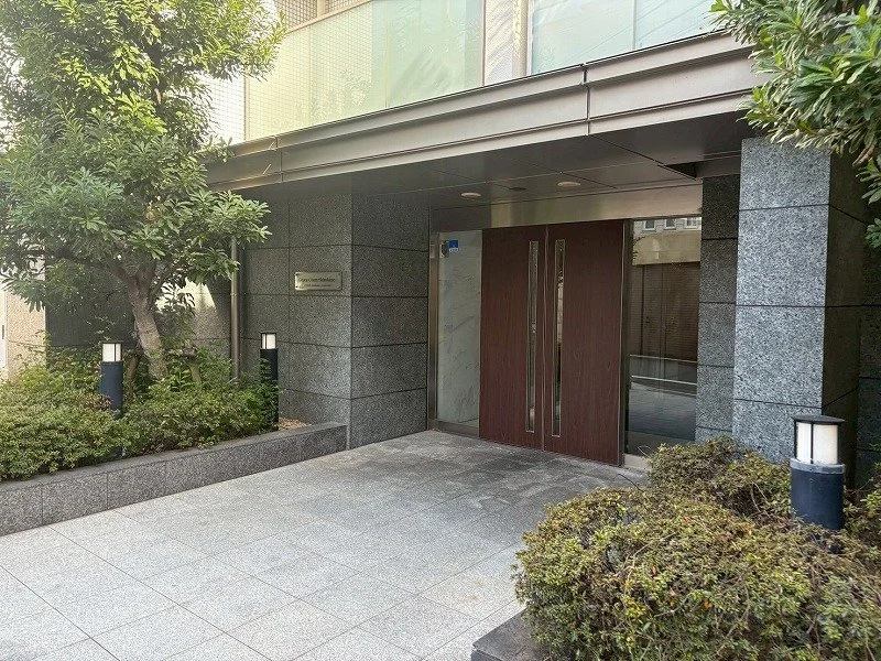 高層ビルのエントランス入口。木製のドアと照明付きの植栽が見える。