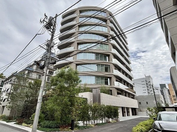 高層のコンクリート建築のマンションが描かれた都市景観。道路と電柱、木々と車も見える。