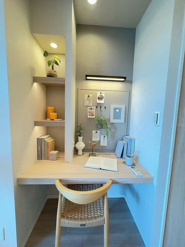 木製のデスクとチェア、小さな棚に植物や本、メモ帳、色とりどりの装飾品が置かれたシンプルな作業スペース