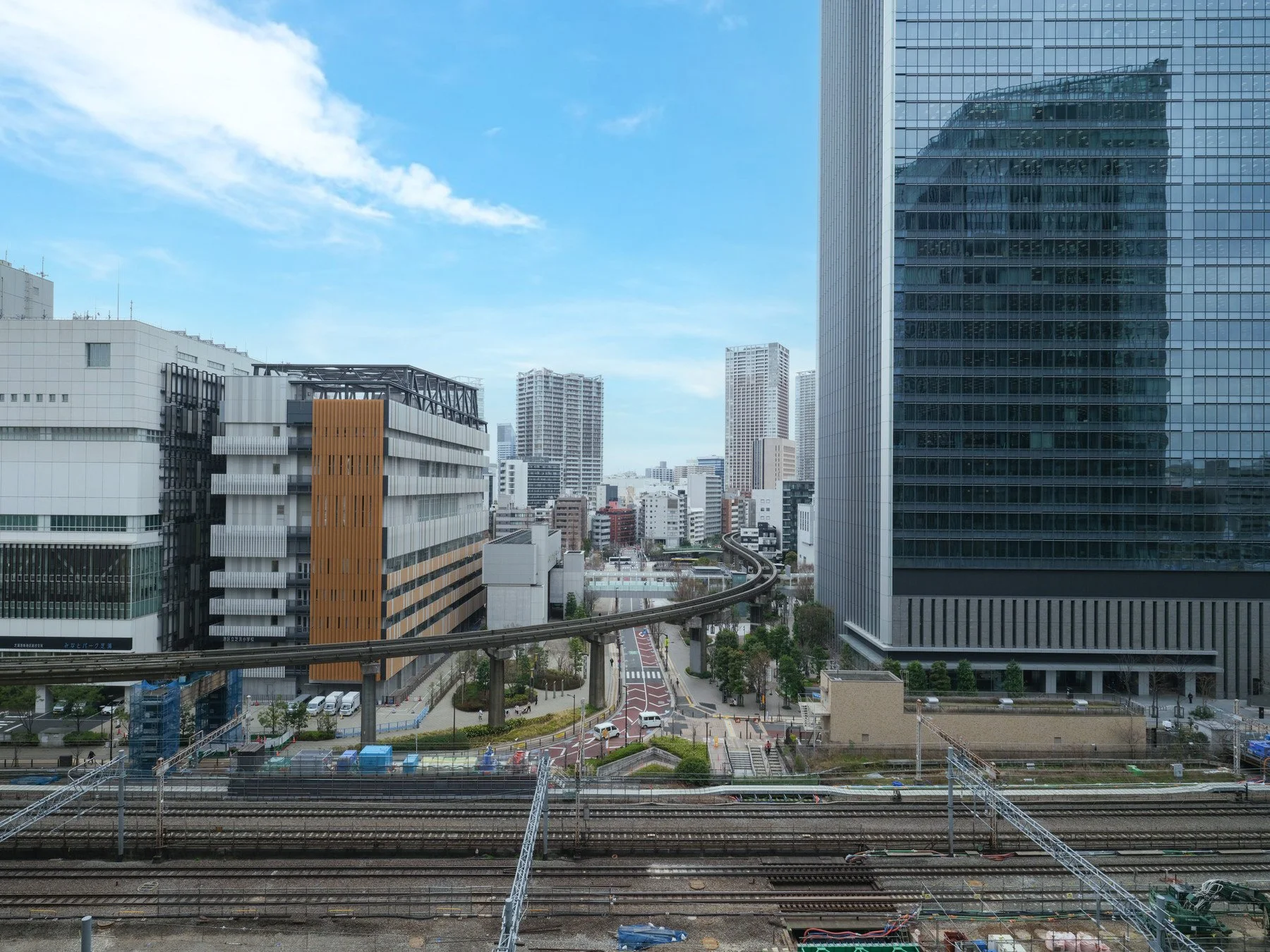都市の景色。高層ビル群と鉄道線路が交差している。青空と散らばる雲。多くの現代的な建物が見える風景。
