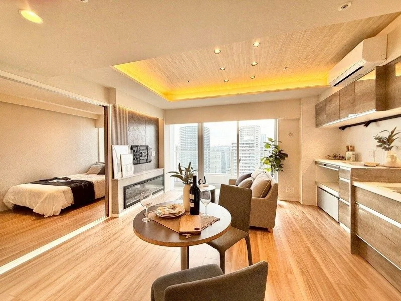 明るい高層マンションのリビングルームと寝室の画像。木製の床と現代的な家具、窓から都市の景色が見える。