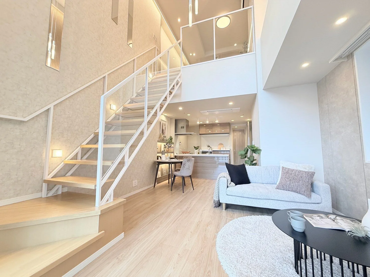 広々としたリビングルーム、白いソファとコーヒーテーブル、階段とリビングダイニングキッチンが見える interior of a spacious modern living room with a white sofa, black coffee table, and staircase.