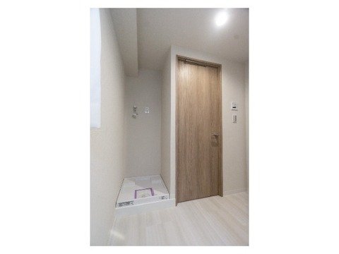 木製のドアと白い壁の室内の一角。左側には窓とコンセント、右側には壁に取り付けられた操作パネルとライトがある。
