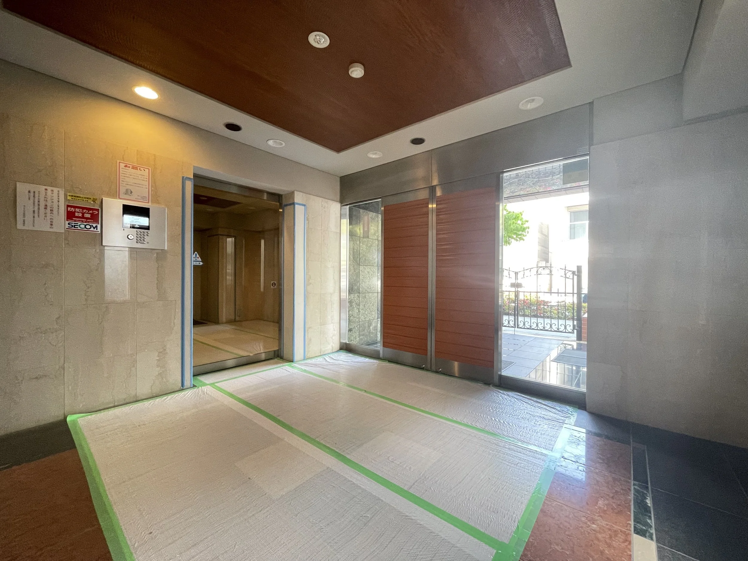 エレベーターの前にカーペットが敷かれている清潔なロビーやエントランスエリア。右側にはガラス扉と外の景色が見える。