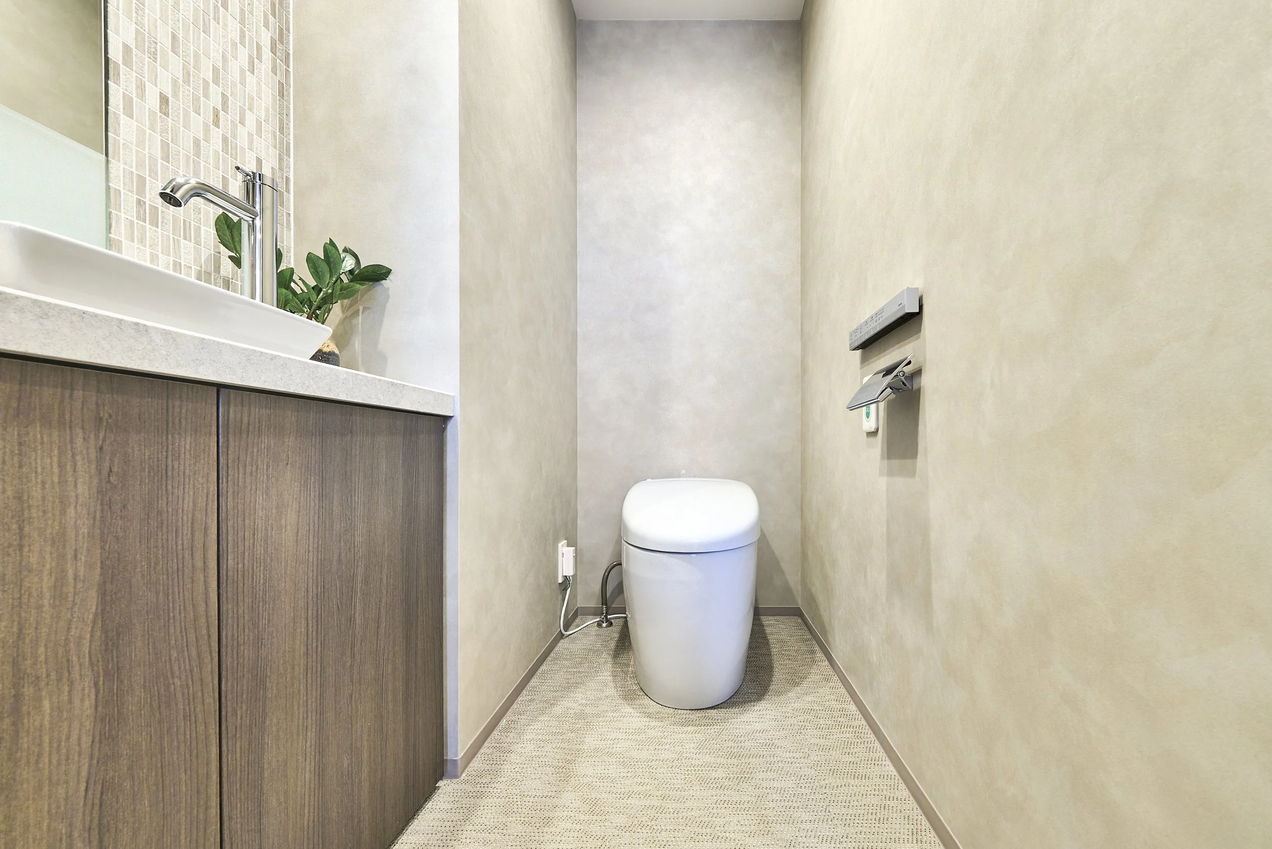 コンパクトなトイレルーム、白色の便器と木目調の収納キャビネット、シンクと緑の植物がある