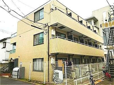 三階建ての黄色いマンション。バルコニーと窓があり、フェンスで囲まれている。