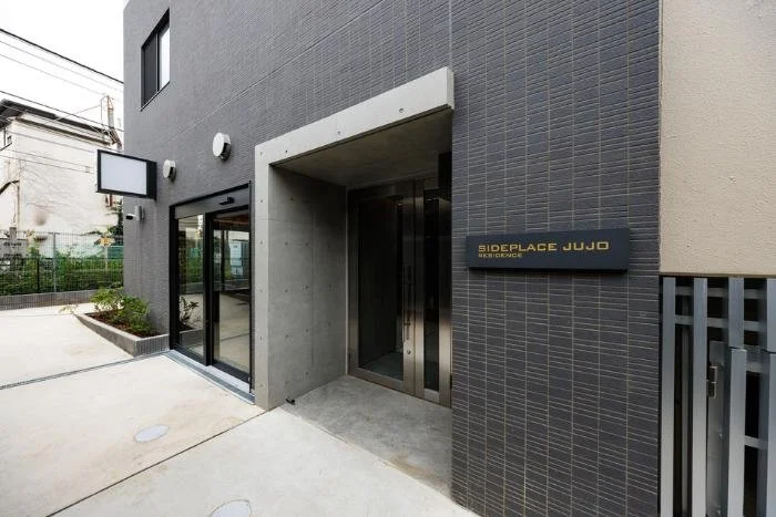 モダンな建物の入り口。黒いタイルの外壁と金属製のドアが見える。