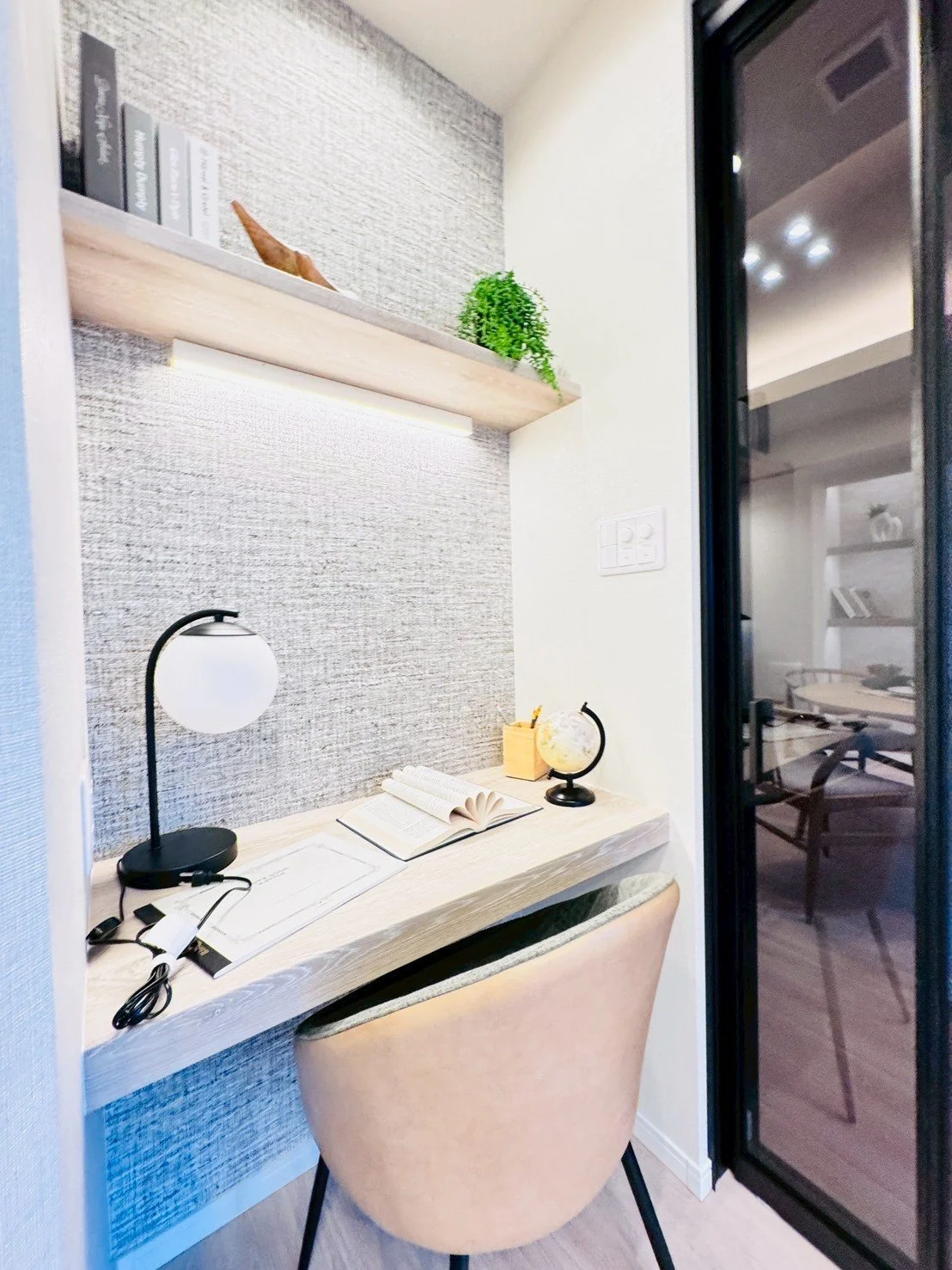 デスクと椅子、小さな置き時計と本、ランプと植物が置かれた書斎スペースの写真