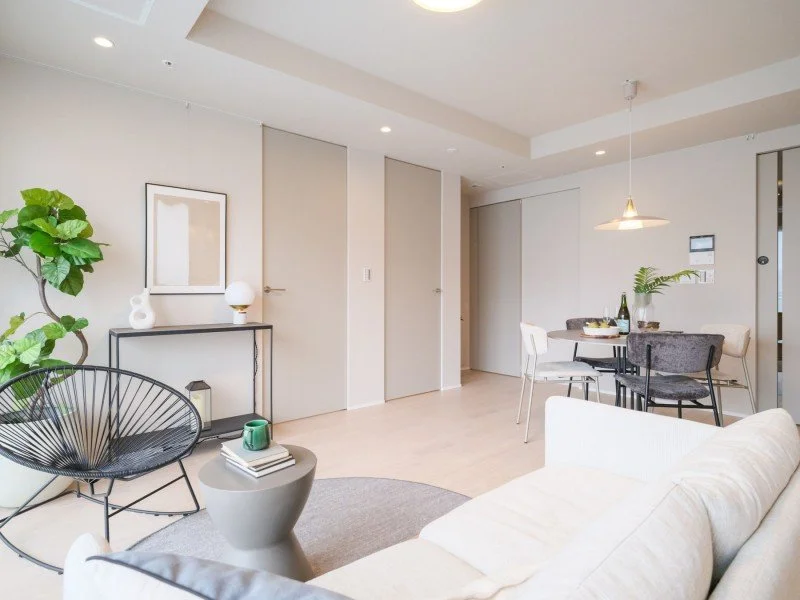 白いソファ、ダイニングテーブルと椅子、観葉植物、壁に絵画や装飾品、シンプルなリビングルームのインテリア