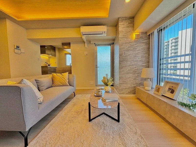 モダンなリビングルームのインテリア。ソファ、コーヒーテーブル、クッション、ランプ、飾り棚、観葉植物と大きな窓から高層ビルが見える風景。