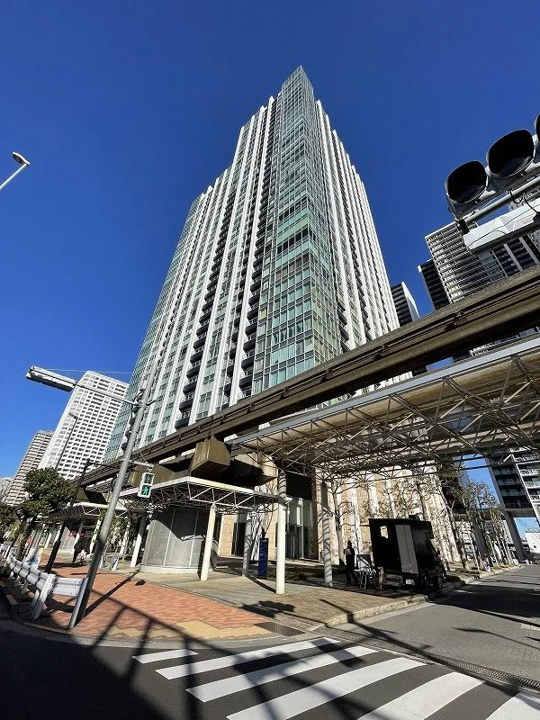 高層ビル街と歩道。青空の下で近代的な建物と道路、横断歩道や人々が写っている。