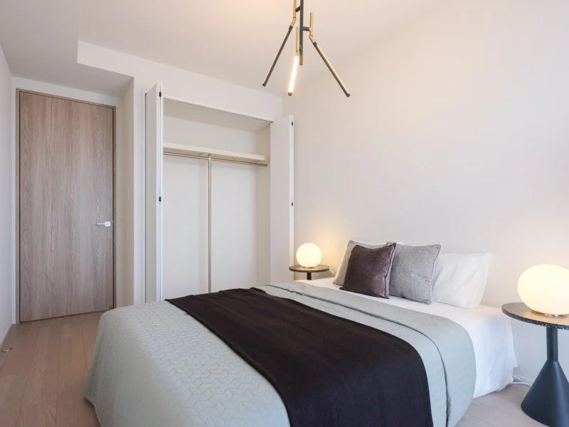 白いベッドと枕、サイドテーブルに丸いランプ、開いたクローゼットと木製のドアがあるシンプルな寝室のインテリア